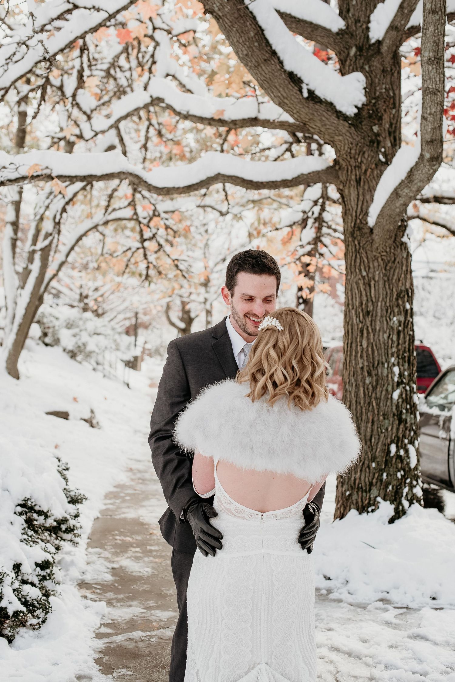 Bride in white gown with fur shawl and groom in dark suit share a romantic moment on a snowy winter wedding day.