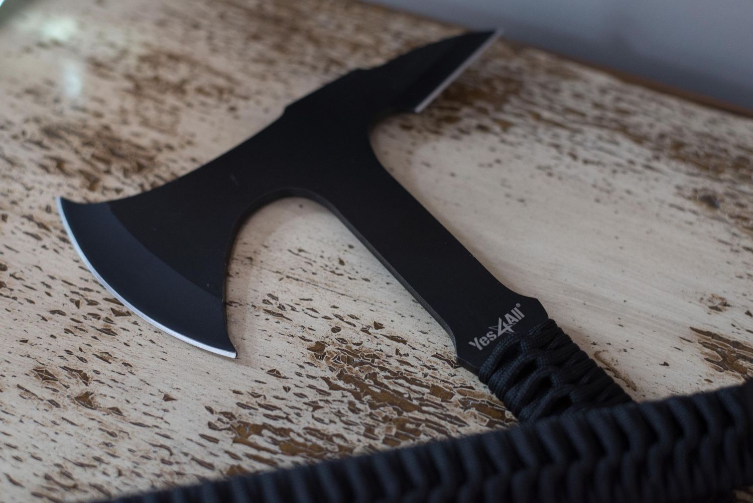 Black tactical tomahawk axe with paracord handle displayed on a wooden surface, featuring a sharp blade edge.