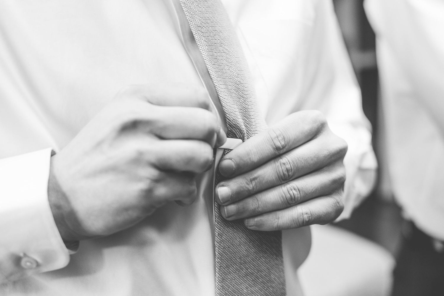 Black and white close-up of a man adjusting his tie, wearing a white dress shirt, perfect for wedding or formal event.