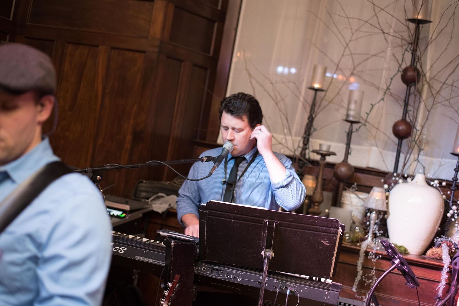 A musician plays keyboard and sings into a microphone at an elegant indoor venue with candlesticks and decor.