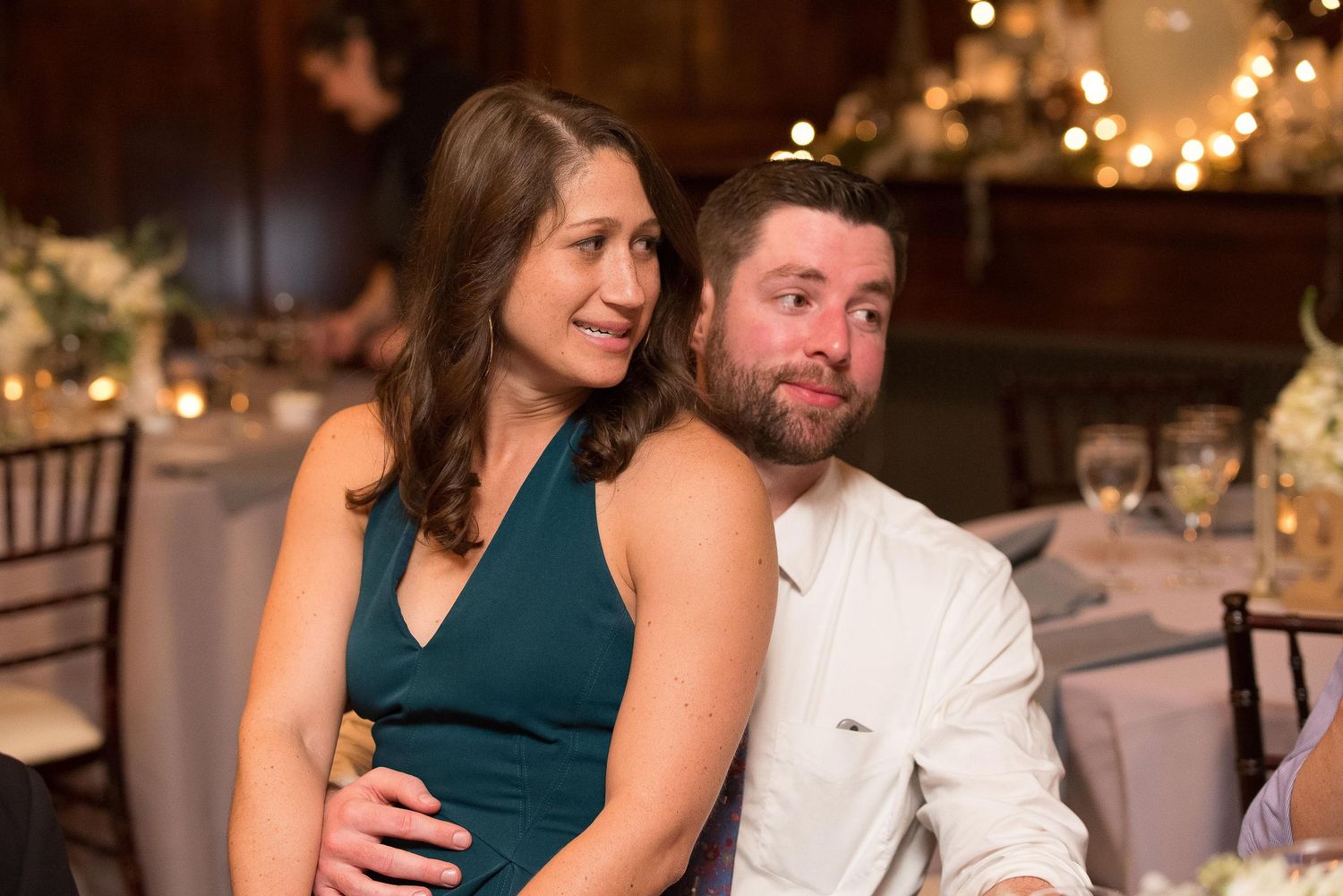 Couple smiling together at a wedding reception, woman in teal dress, man in white shirt, warm bokeh lights.