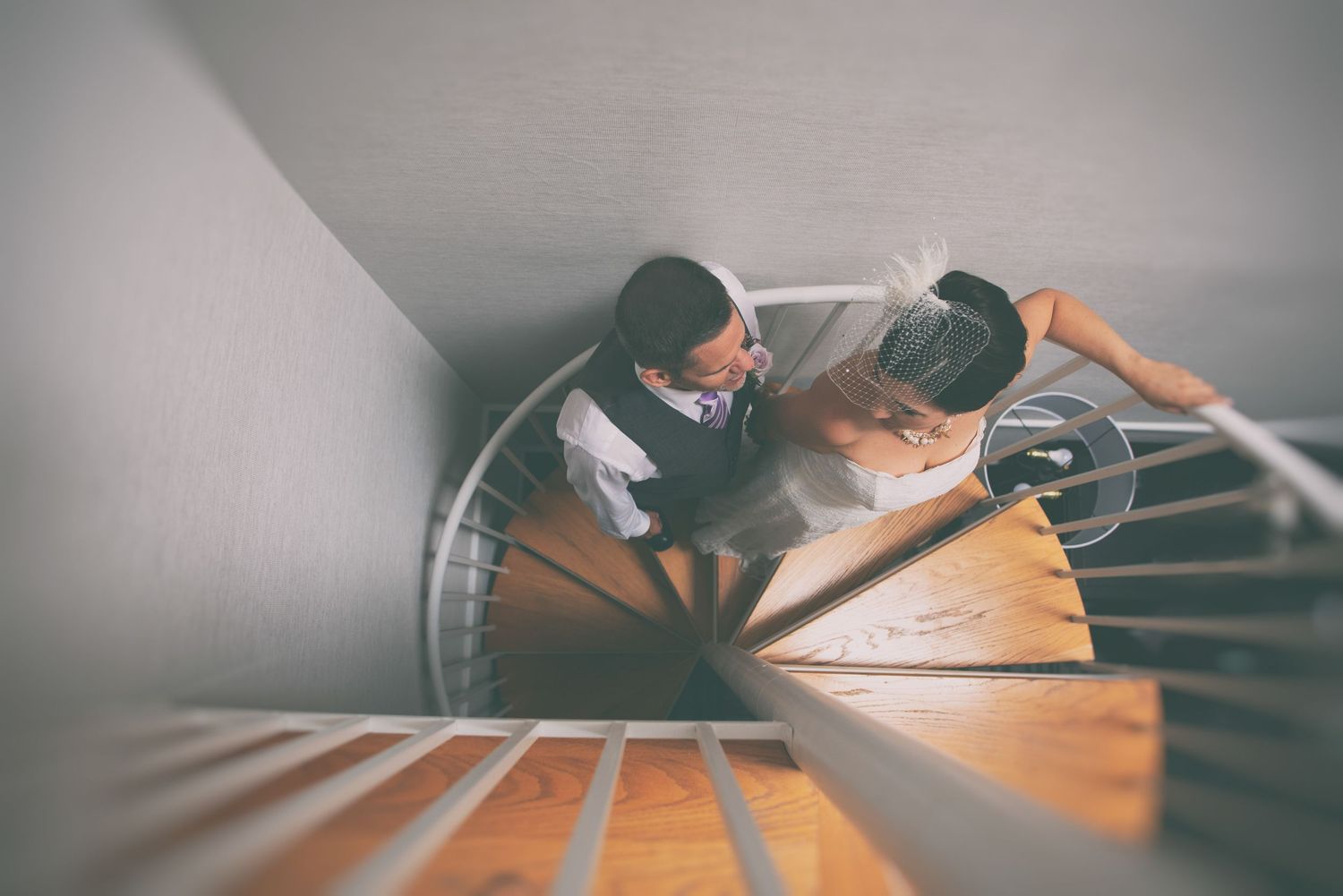 Couple sharing a romantic moment on a wooden spiral staircase viewed from above.