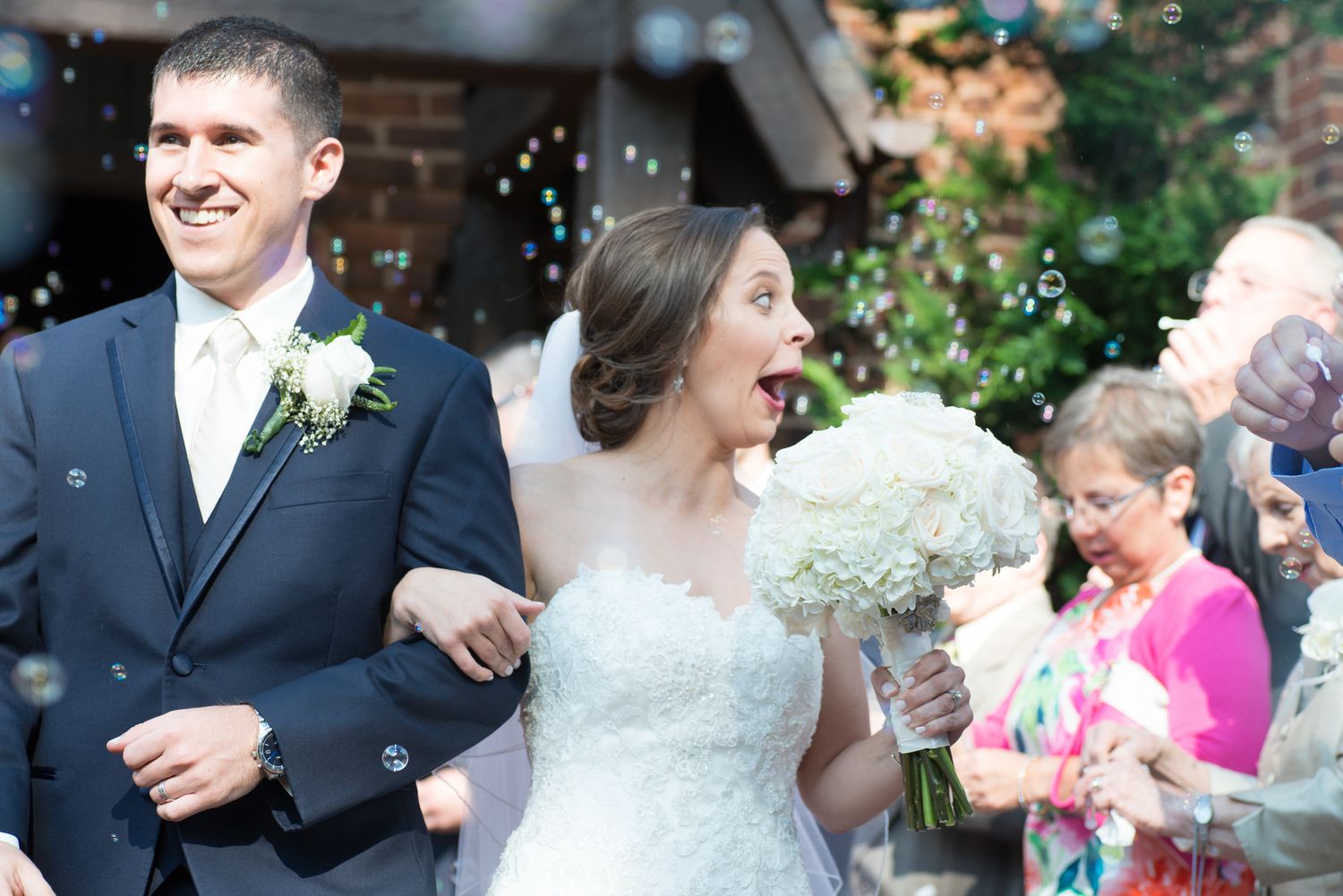 Bride reacts with surprise and joy as bubbles surround the couple during their wedding reception exit celebration.