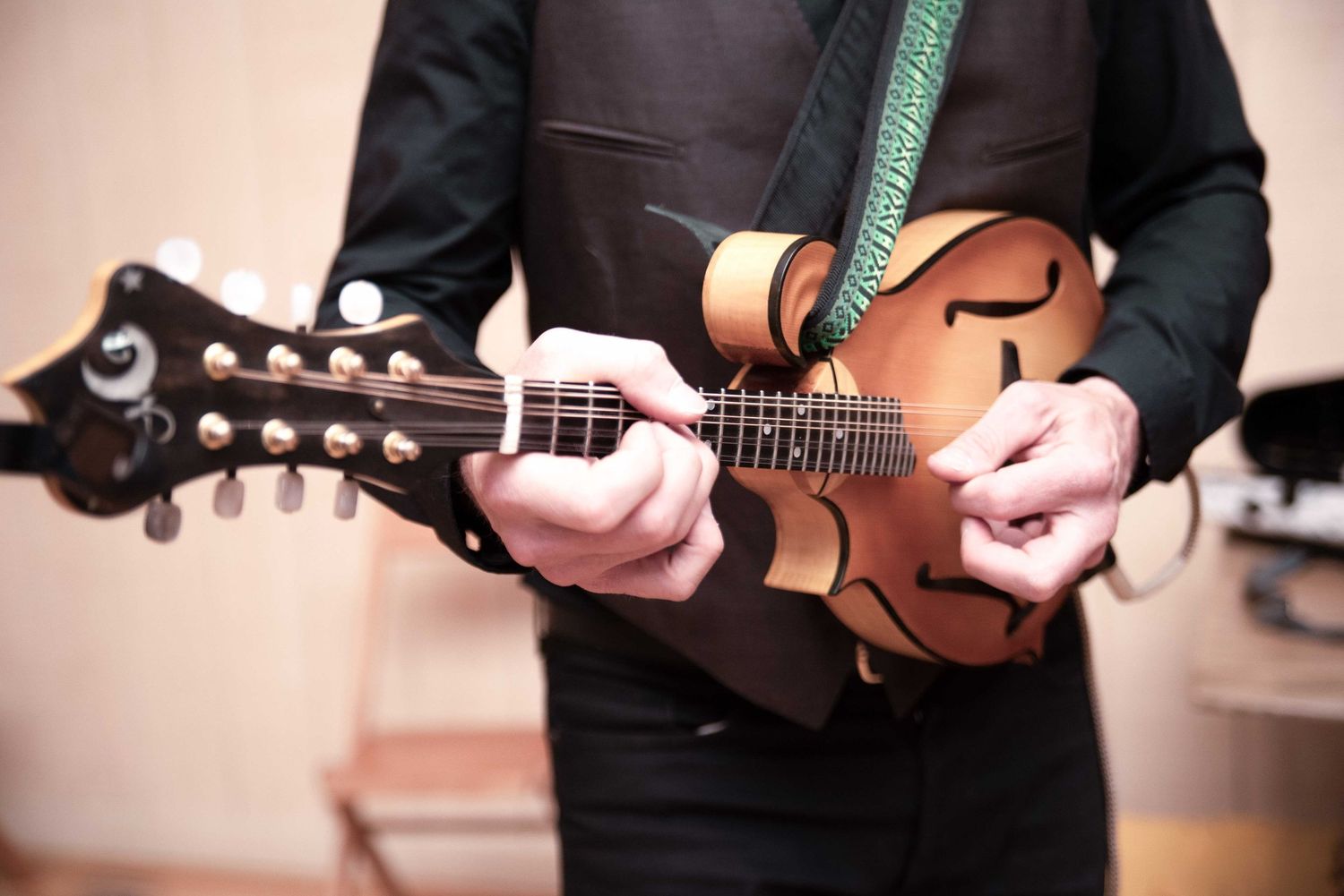 Close-up of a musician playing a mandolin with a green strap at a wedding reception.