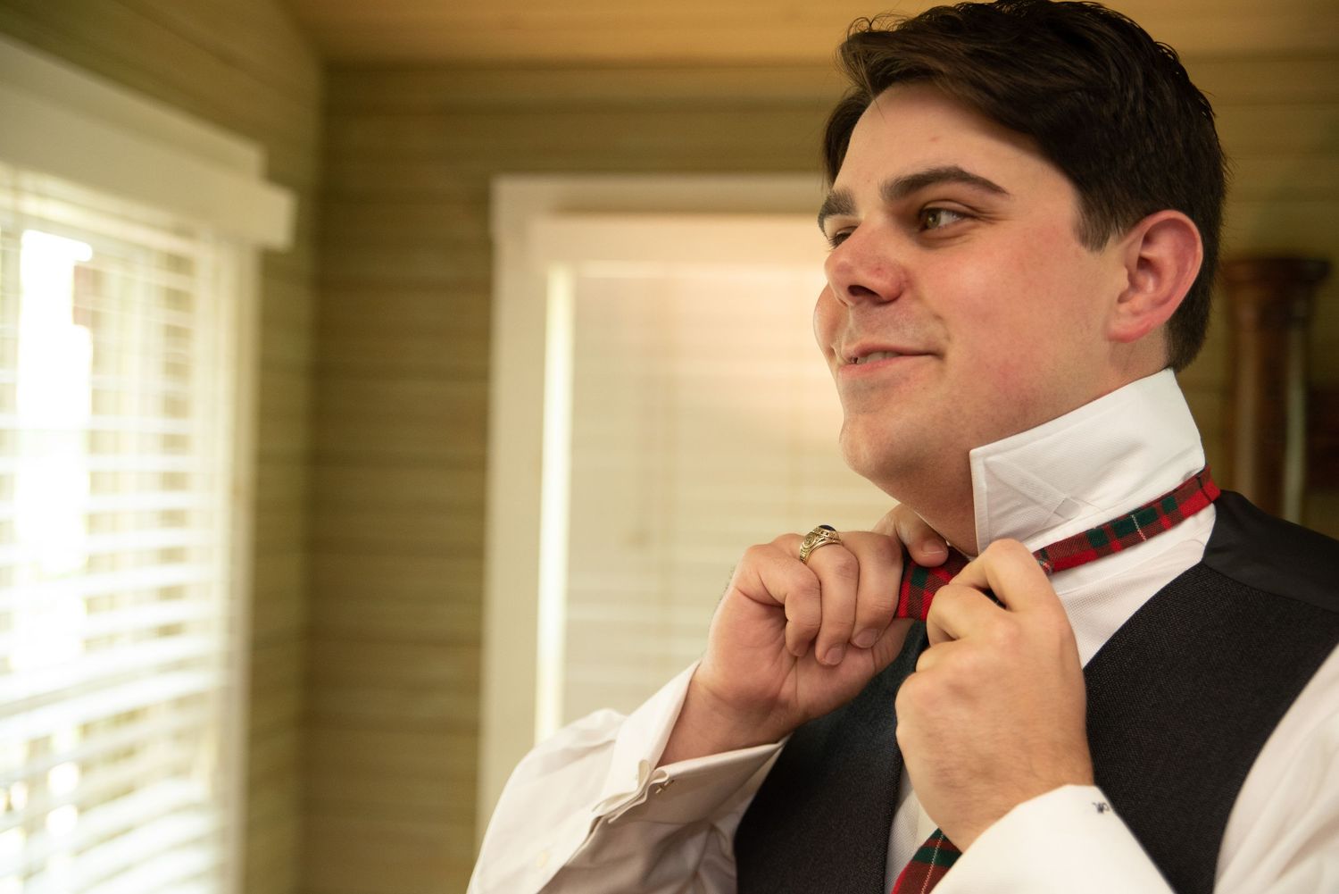 Groom in gray vest adjusting plaid bow tie while getting ready for wedding.