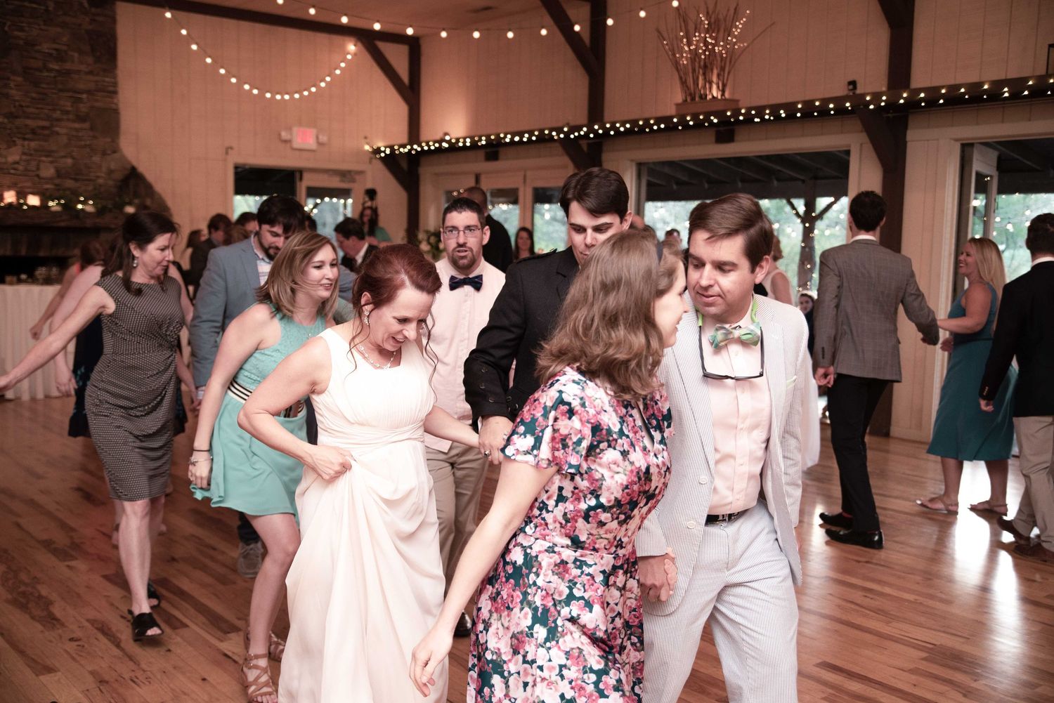 Wedding guests dancing joyfully at a rustic barn reception venue with string lights and wooden decor.