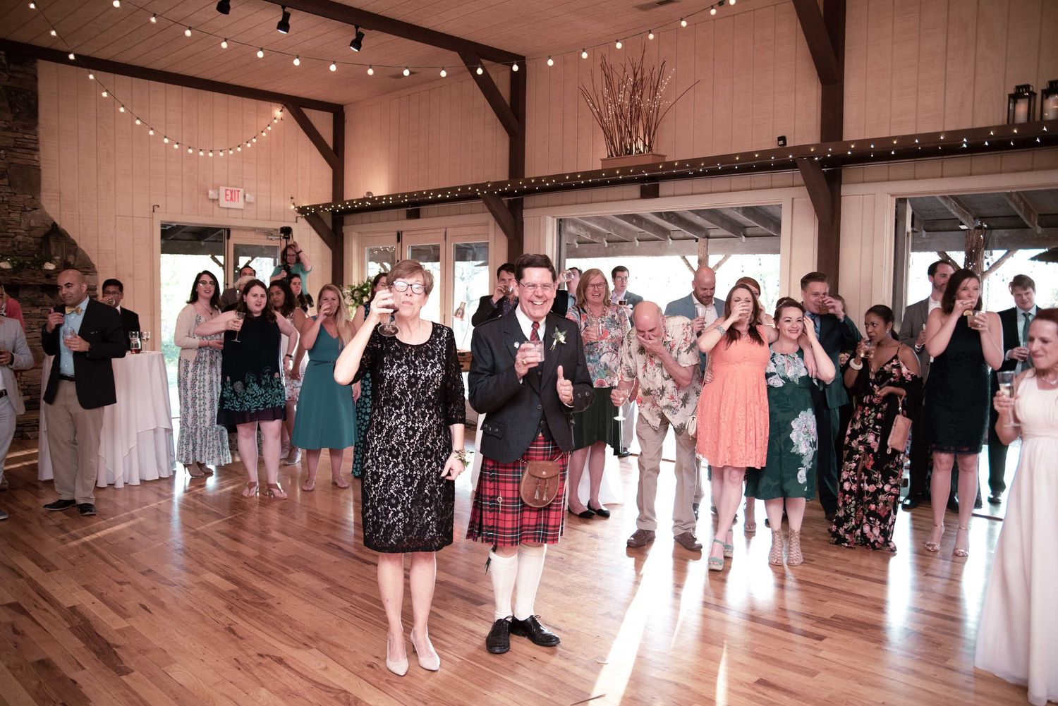 Wedding reception guests celebrating in a rustic barn venue with string lights and hardwood floors.