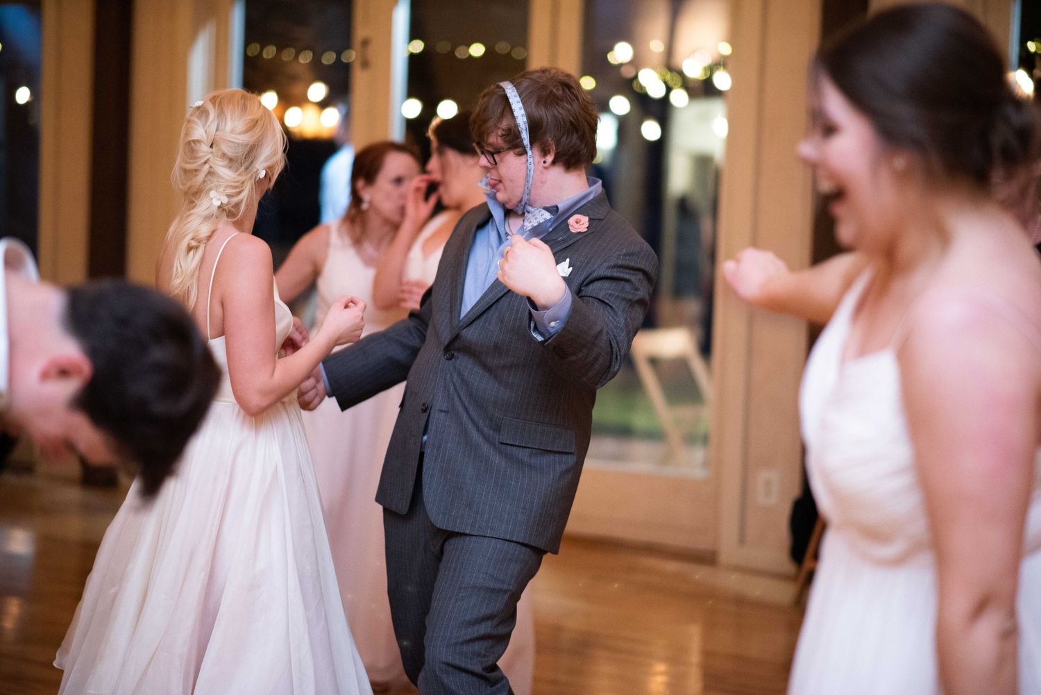 Guests dancing joyfully at a wedding reception in an elegant venue with warm string lights.