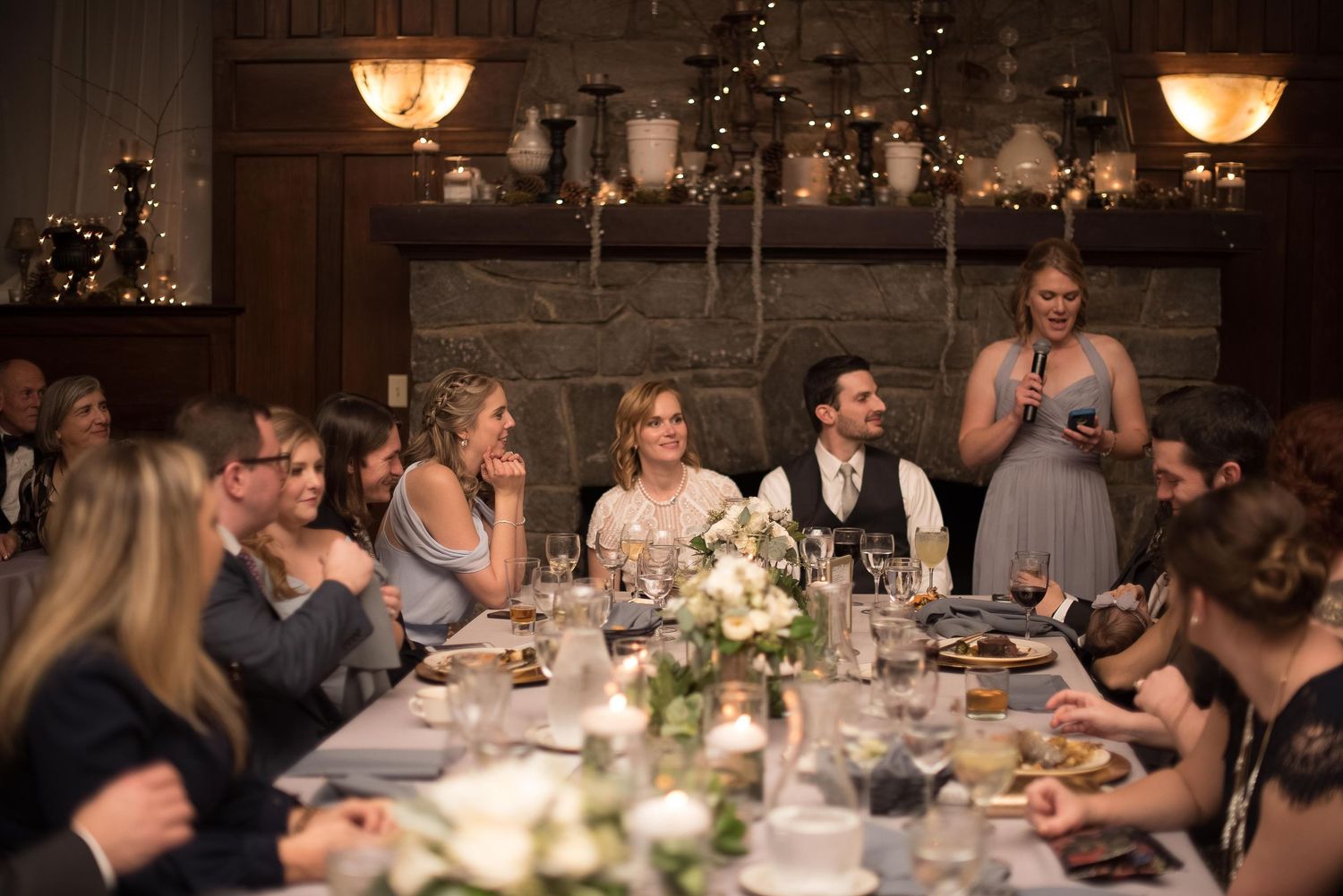 Elegant wedding reception dinner with guests seated at a long decorated table in a warmly lit venue.
