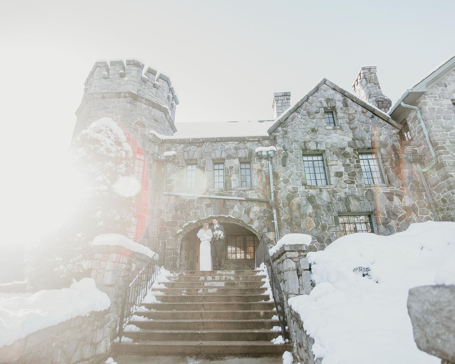 Snow-covered stone castle with grand staircase entrance shrouded in winter fog and mist.