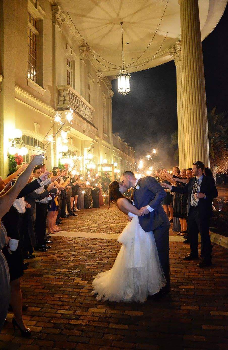 Bride and groom share romantic dip kiss during sparkler send-off exit at elegant night wedding venue.