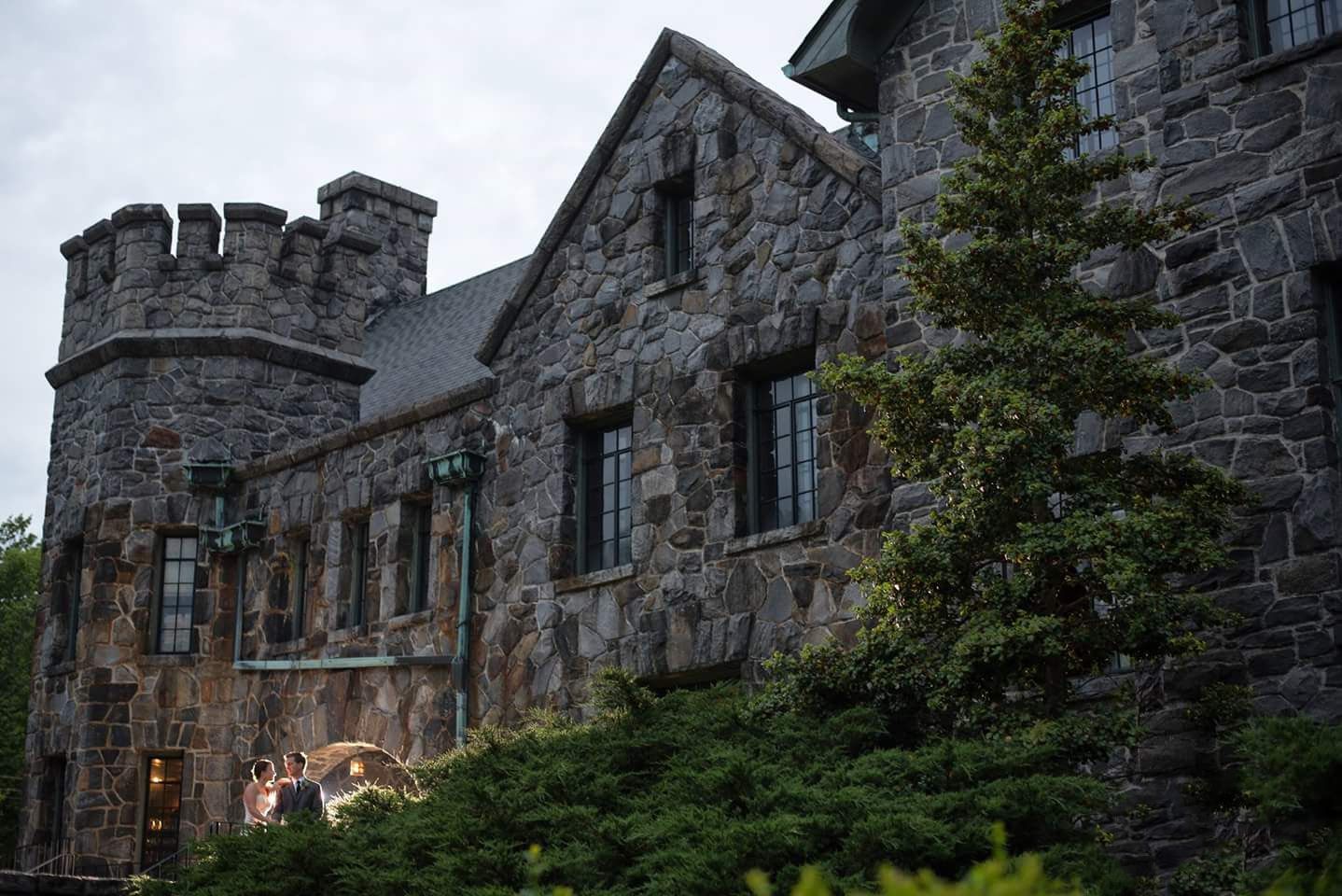 Gothic stone castle wedding venue exterior surrounded by evergreen trees at dusk.