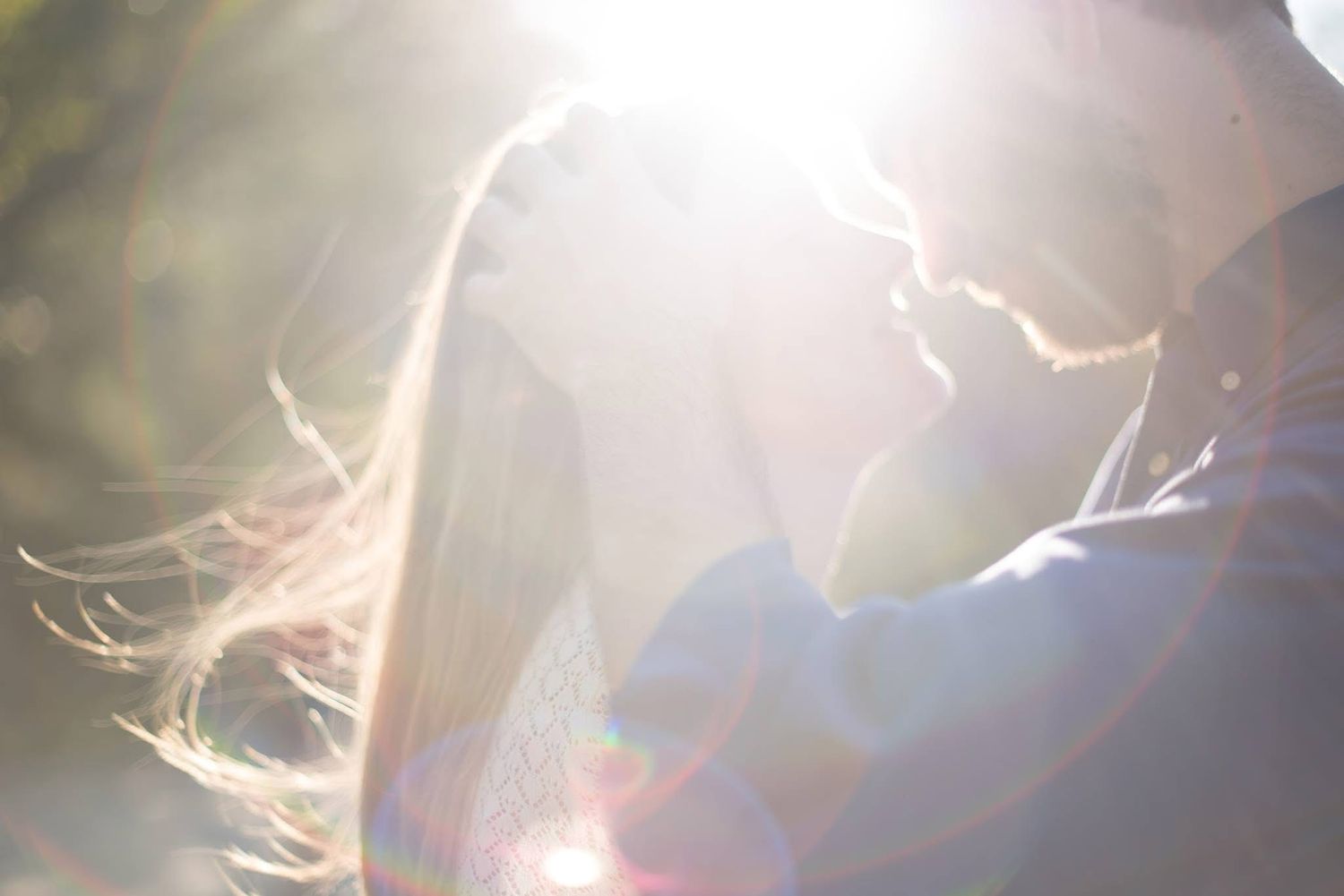 Romantic couple silhouetted in soft golden sunlight during dreamy outdoor engagement photo session.