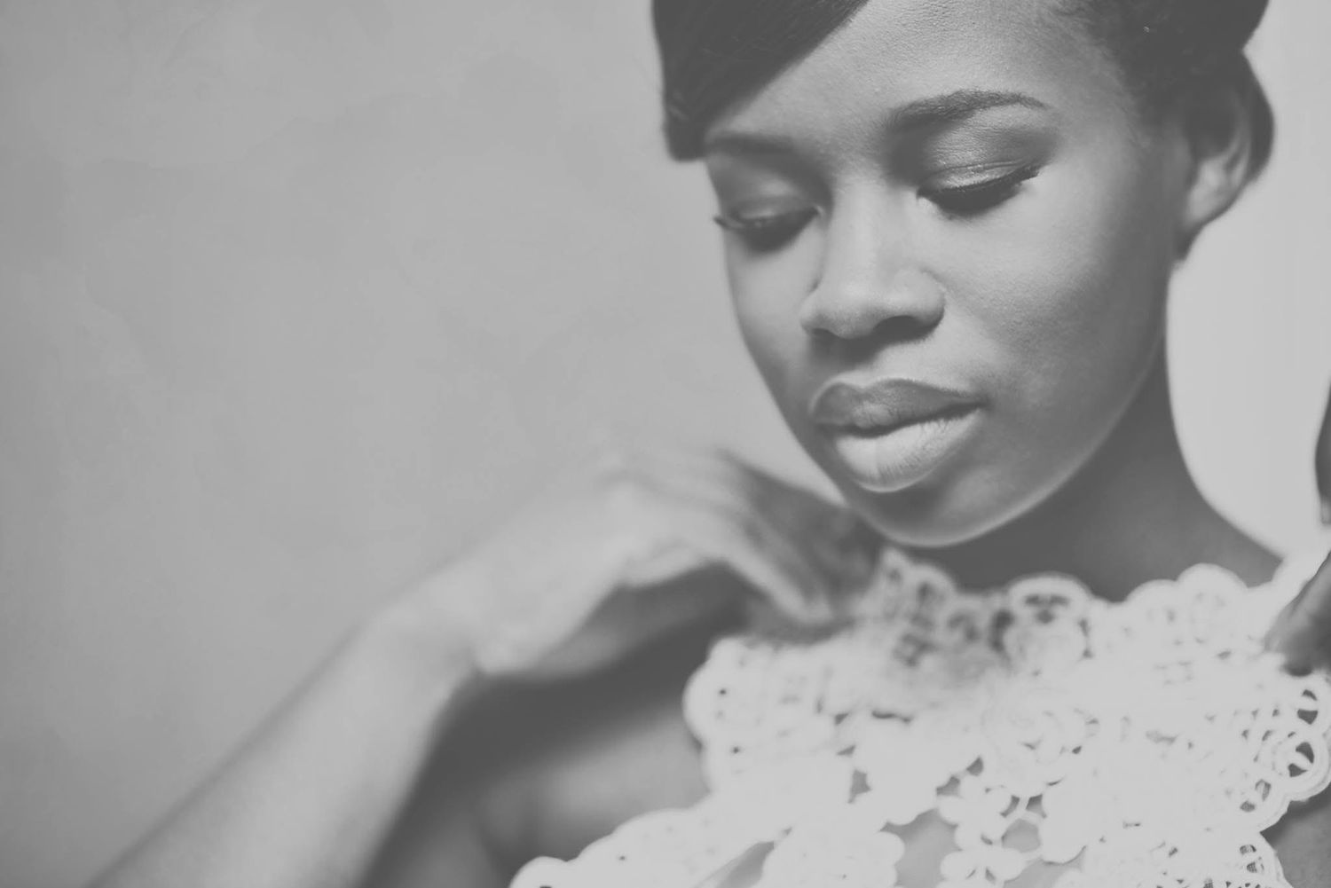 Elegant black and white portrait of bride in lace gown looking down holding bridal bouquet.