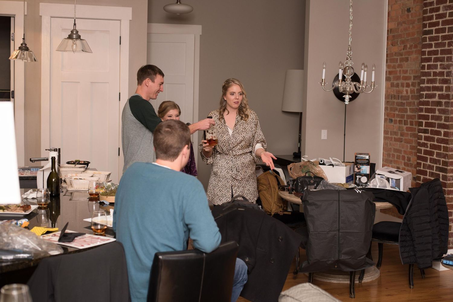 Group of adults socializing in a modern apartment dining area with wine bottles and chandelier lighting.