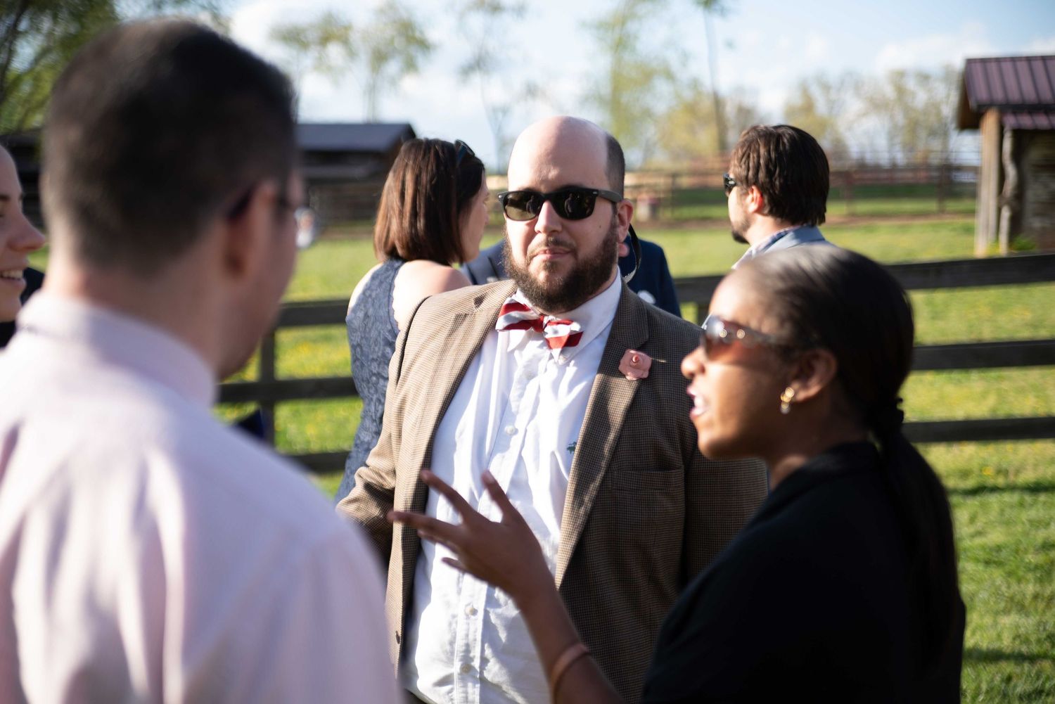 Man in bow tie and sunglasses socializing outdoors at a farm wedding event.