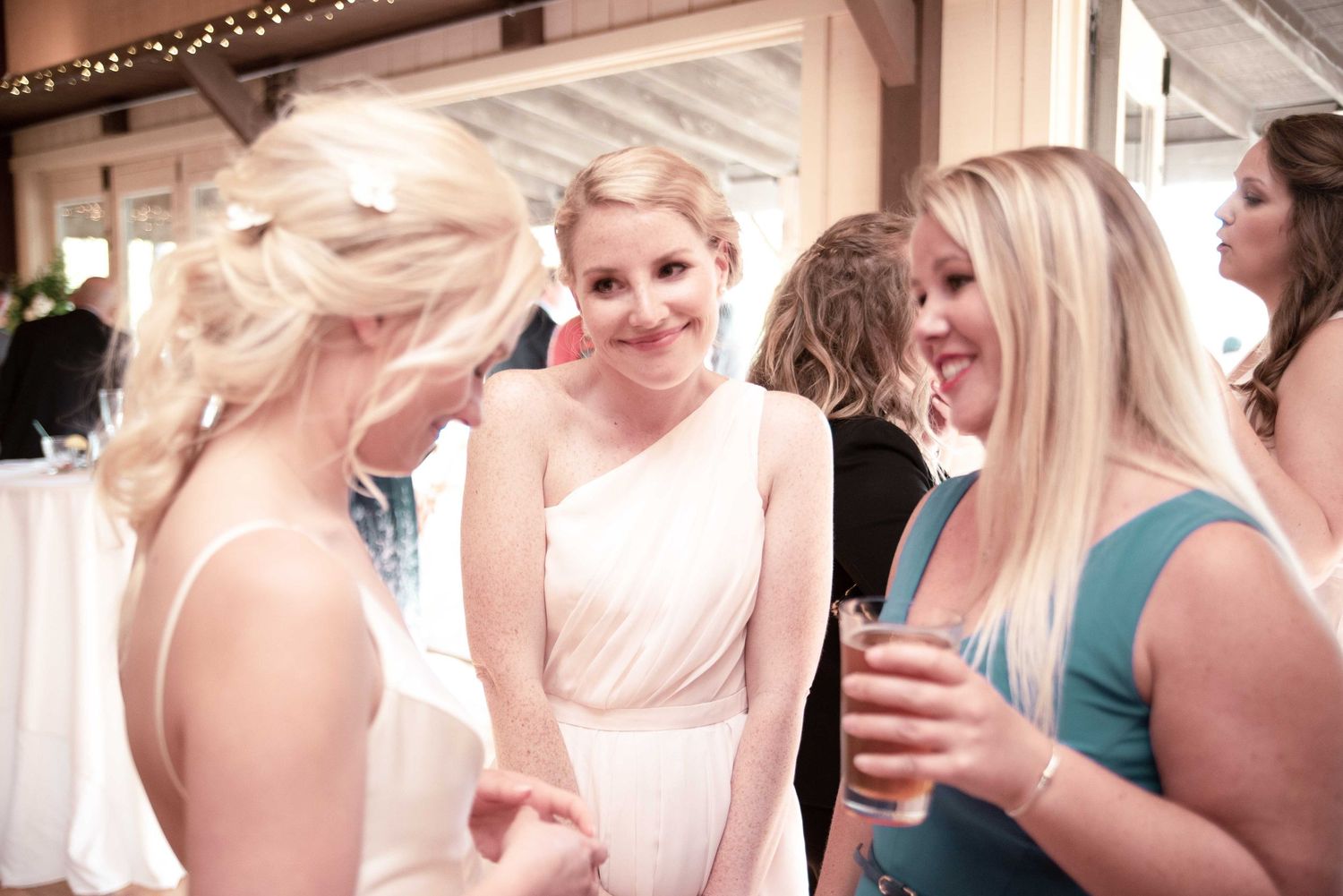 Bride in white dress laughing with bridesmaids in teal at elegant wedding reception.