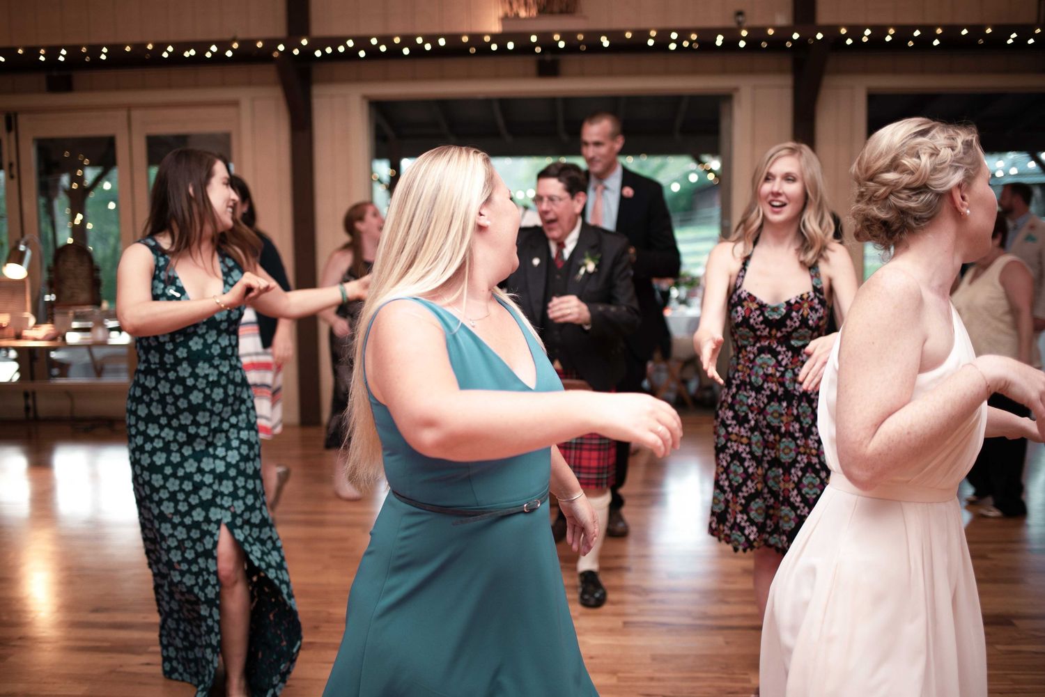Guests dancing joyfully at a wedding reception in an elegant venue with string lights overhead.
