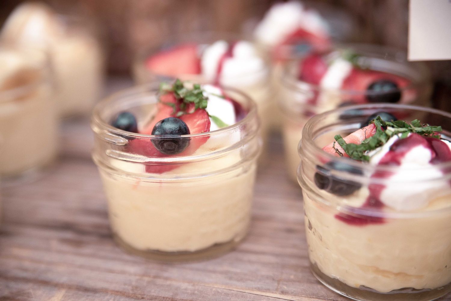 Individual glass cups of creamy dessert topped with fresh strawberries, blueberries, and whipped cream on a wooden table.