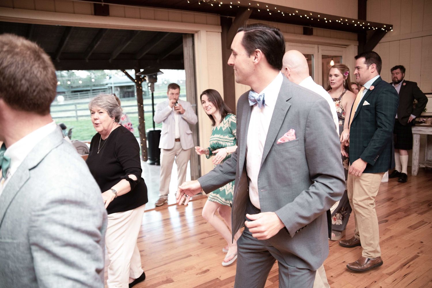 Guests dancing and socializing at an elegant indoor wedding reception venue with wooden beams.