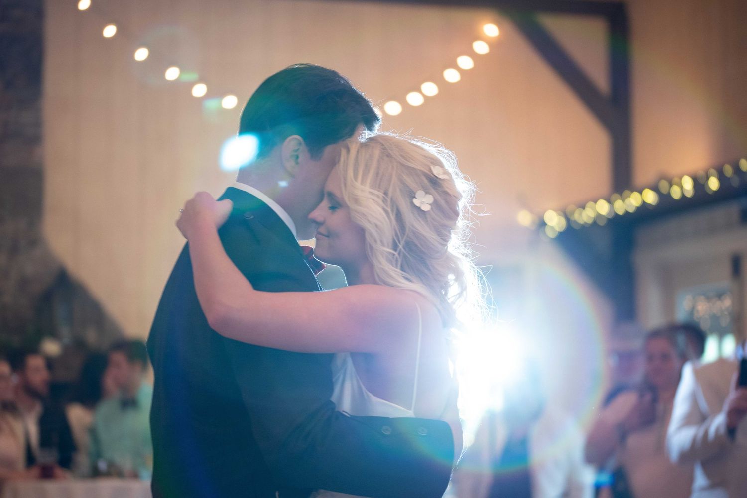 Couple shares romantic first dance at wedding reception with warm string lights glowing in background.