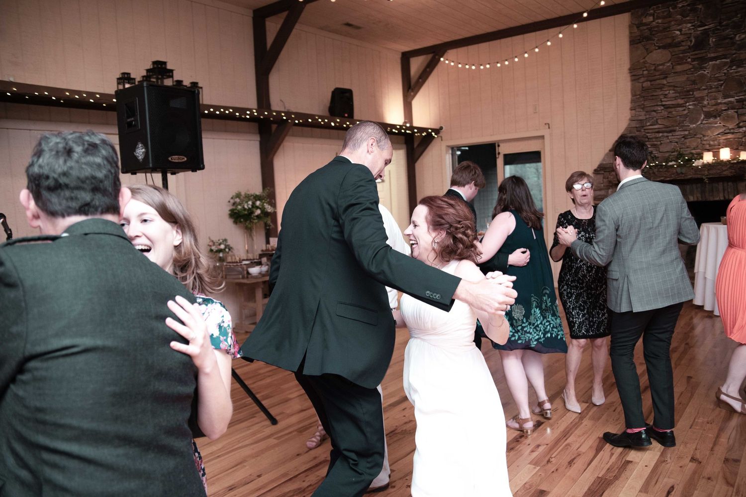 Wedding guests dancing joyfully in a rustic barn reception venue with string lights and hardwood floors.