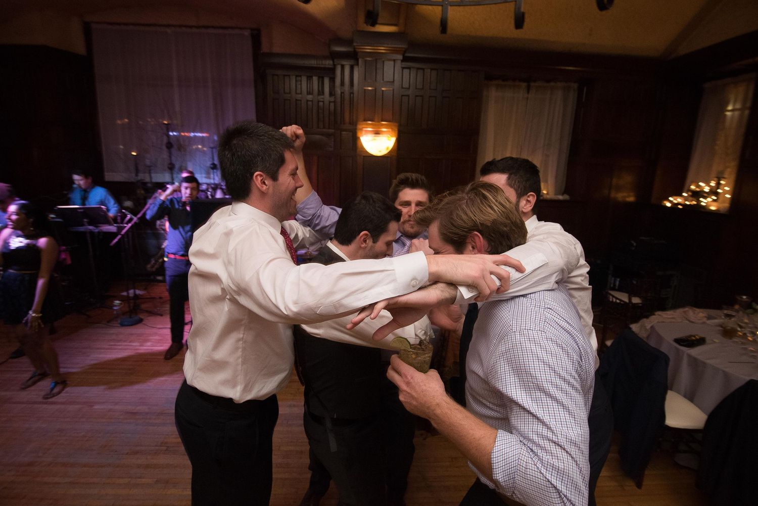Group of young men in dress shirts dancing together at an indoor wedding reception venue.