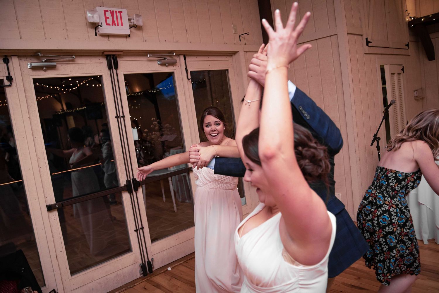 Excited wedding guests dancing and raising hands on the dance floor during a lively reception celebration.