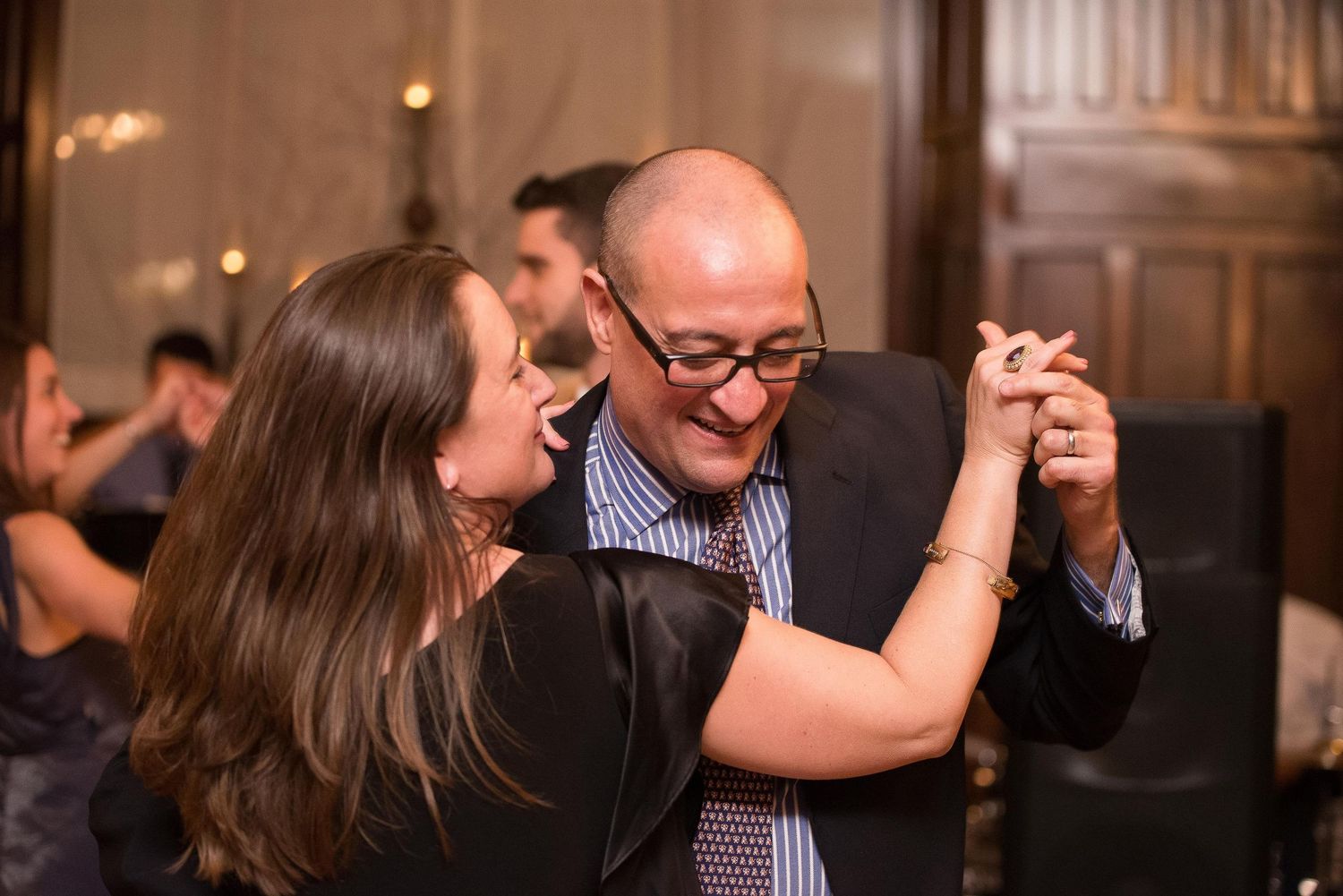 Couple dancing together at an elegant indoor event, smiling and holding hands in formal attire.