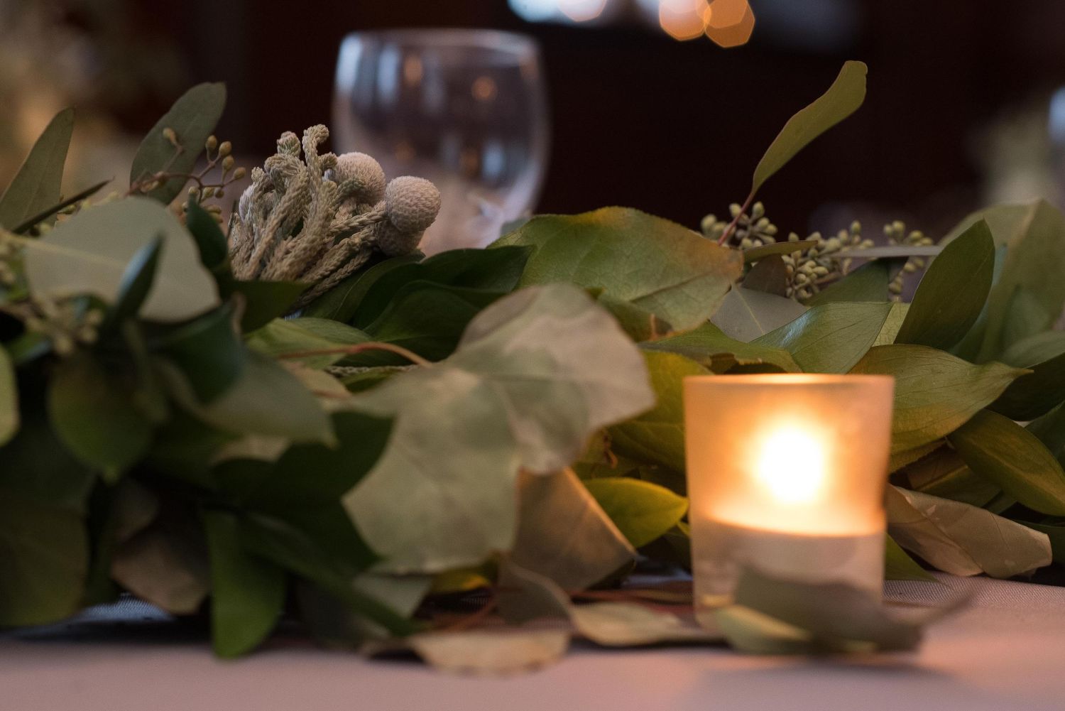 Elegant wedding centerpiece with greenery, eucalyptus, and a glowing votive candle on a reception table.