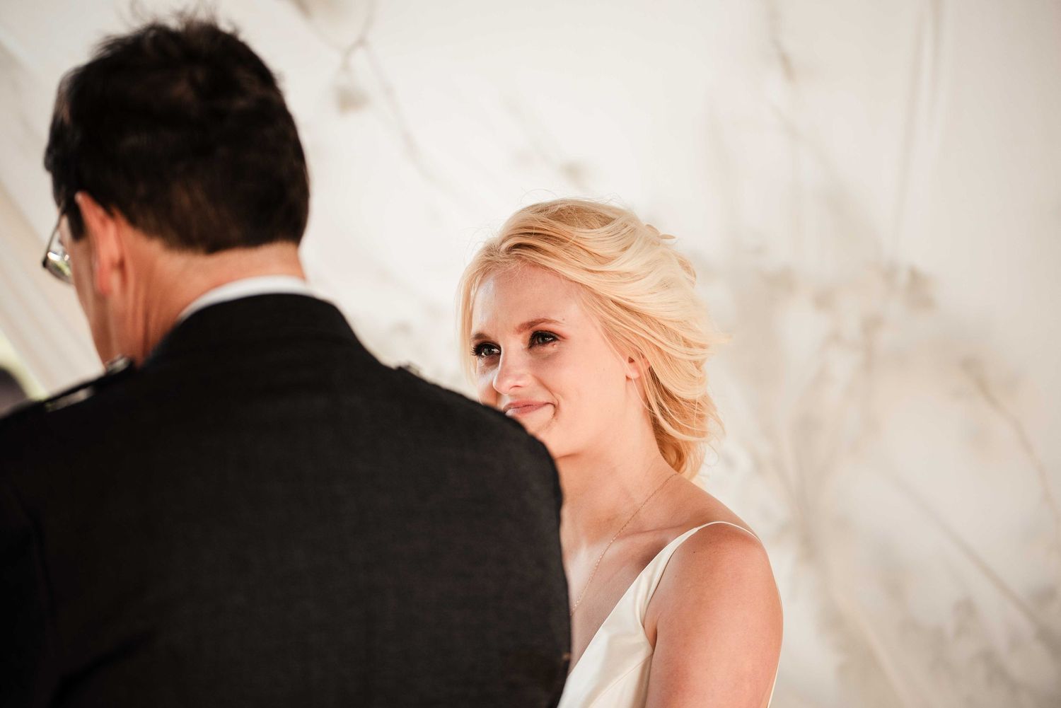 Bride smiling warmly at groom during wedding ceremony with elegant marble background.