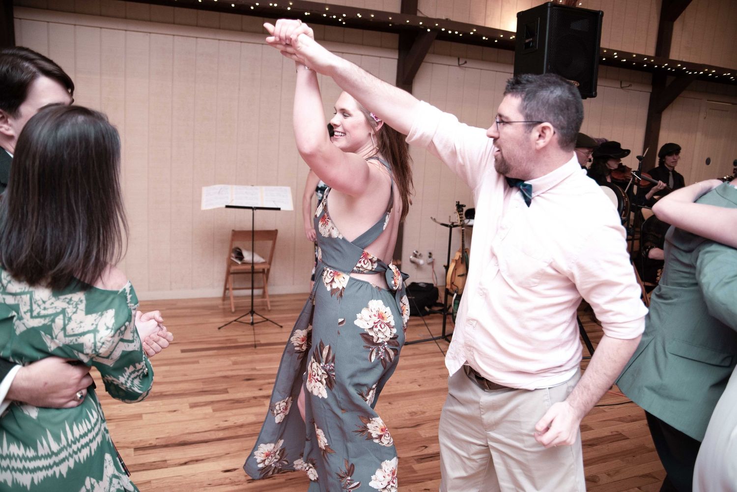 Couples dancing joyfully at a wedding reception on a wooden dance floor with a live band performing in the background.