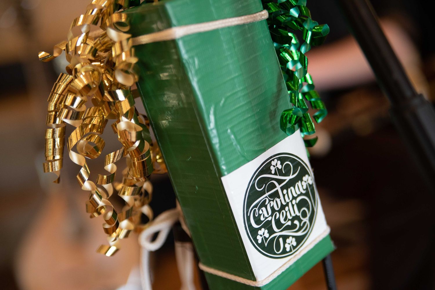 Green gift wrapped in ribbon with gold and green curly bows and a Carolina Crafty label tag.