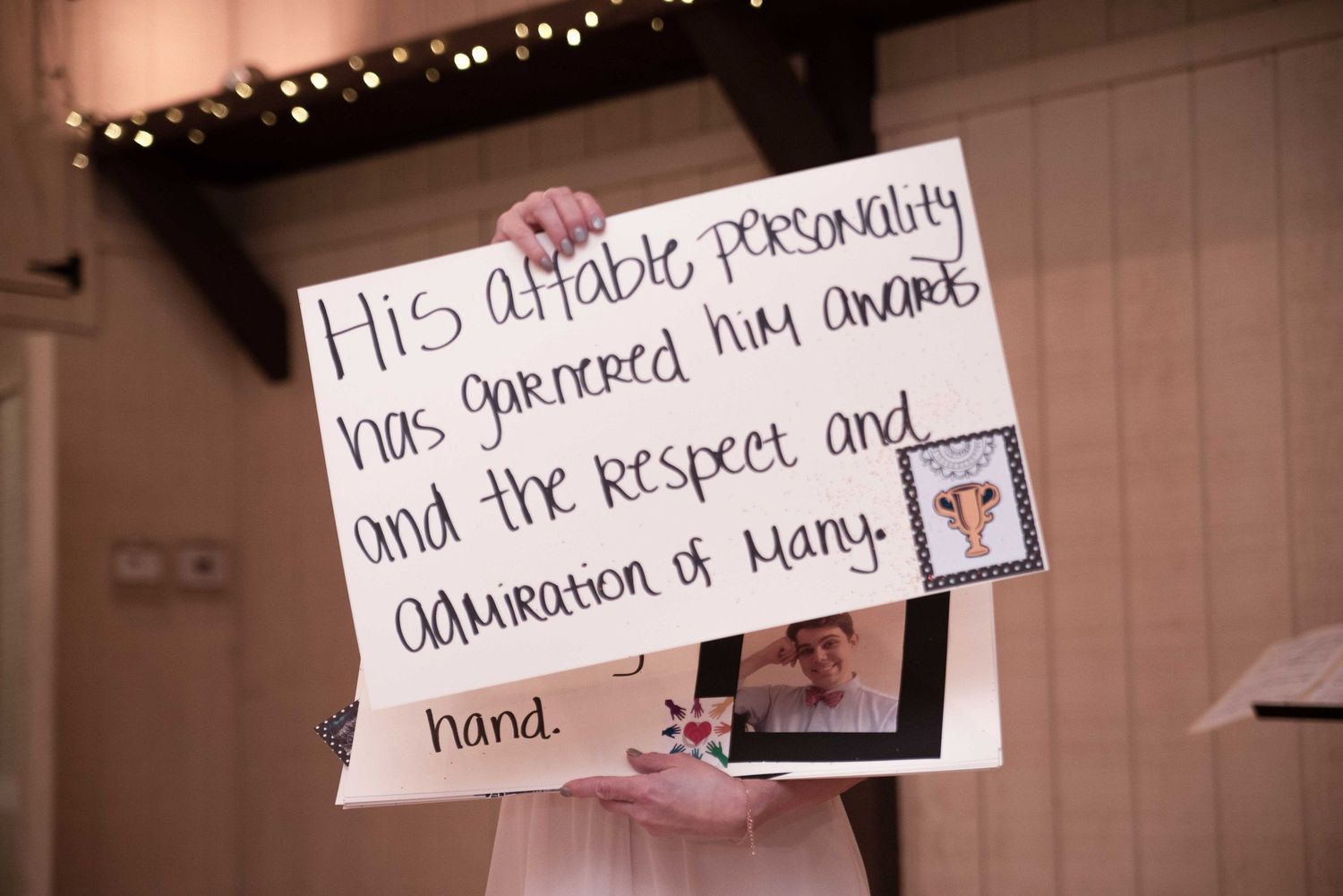 Person holding a handwritten sign praising someone's affable personality, awards, and admiration at a formal event.