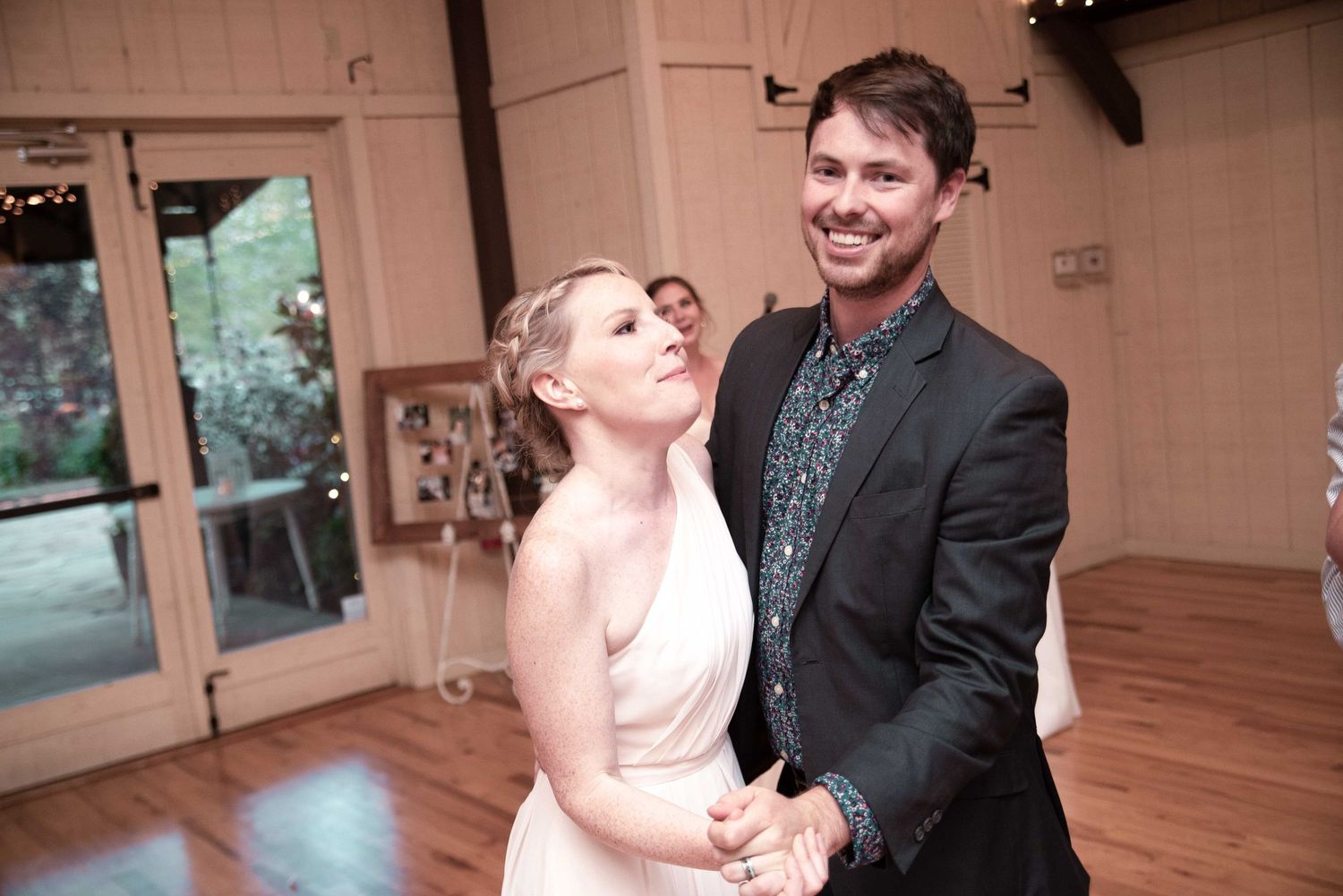 Couple sharing a first dance at a rustic wedding reception, smiling joyfully in elegant attire.
