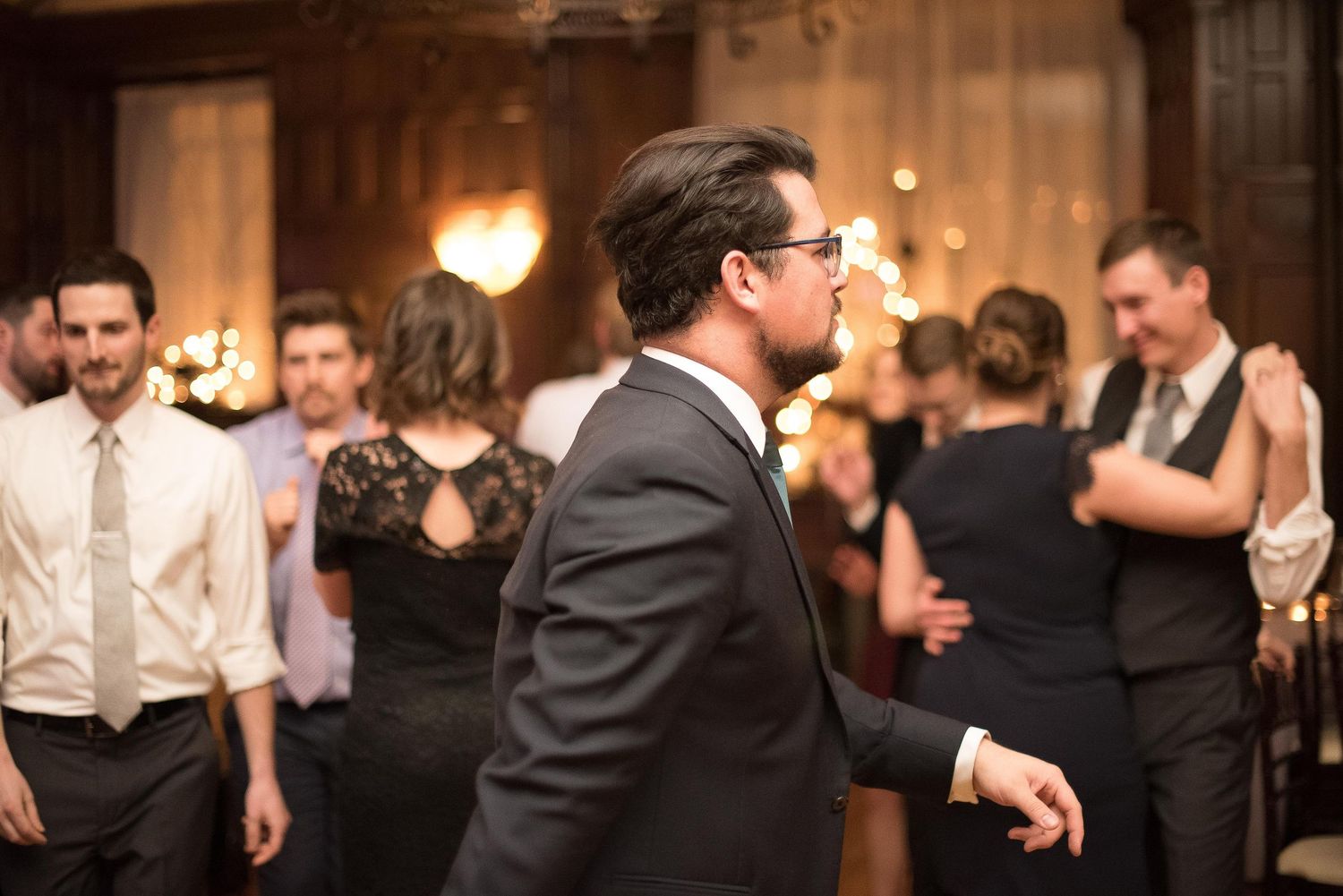 Guests dancing and socializing at an elegant indoor wedding reception in a warmly lit venue.
