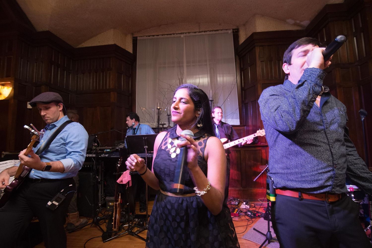 Live band performing indoors, featuring a female vocalist and musicians playing guitar and harmonica on stage.