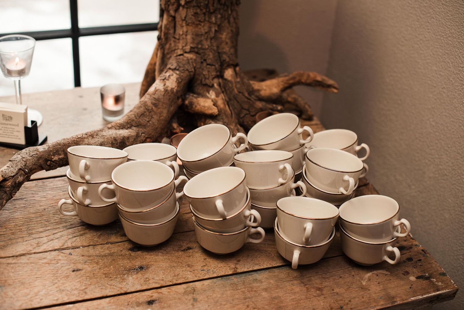 Stacked white ceramic coffee cups arranged on a rustic wooden table near a decorative tree branch centerpiece.
