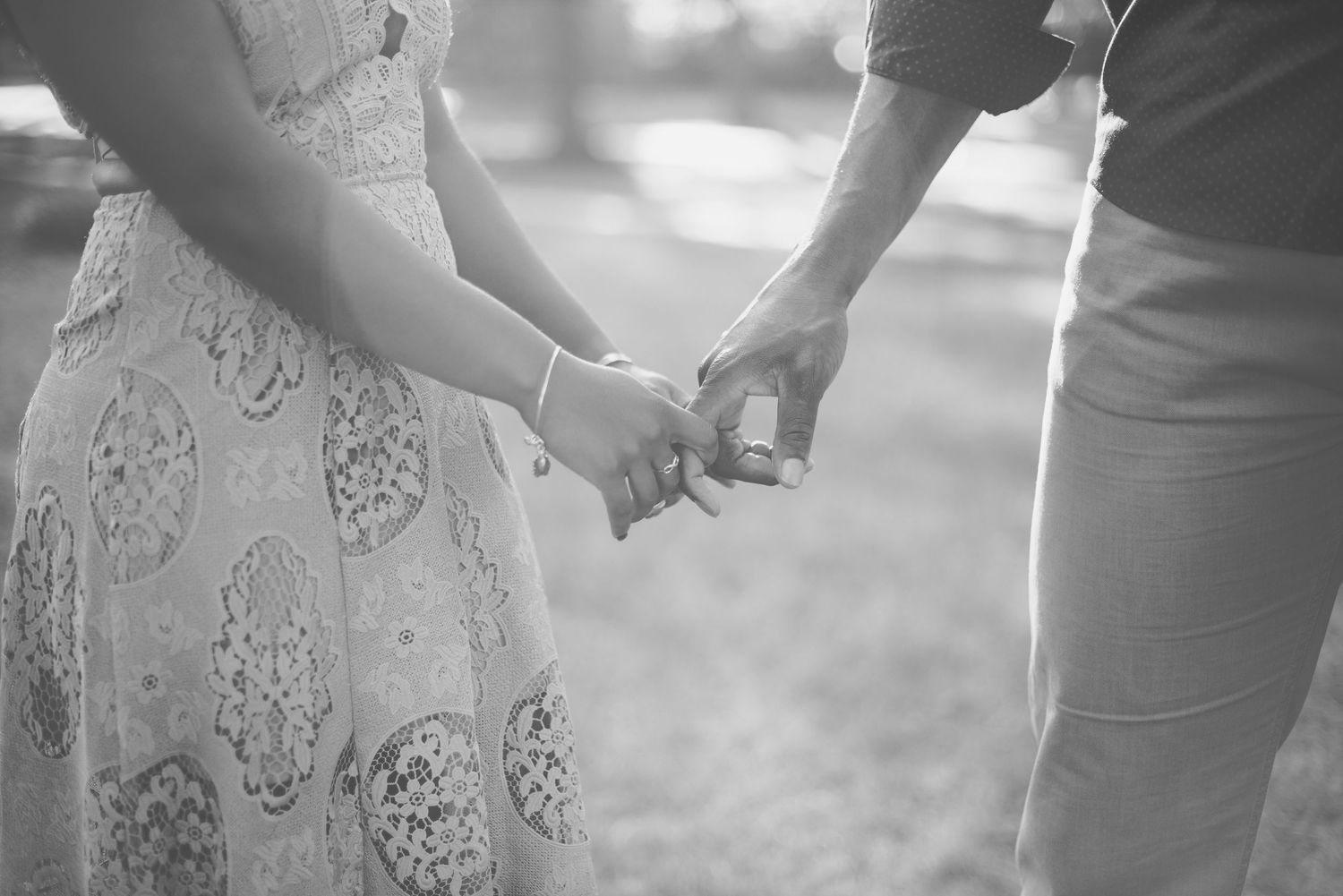 Black and white photo of a couple holding hands outdoors, showcasing a romantic engagement moment.