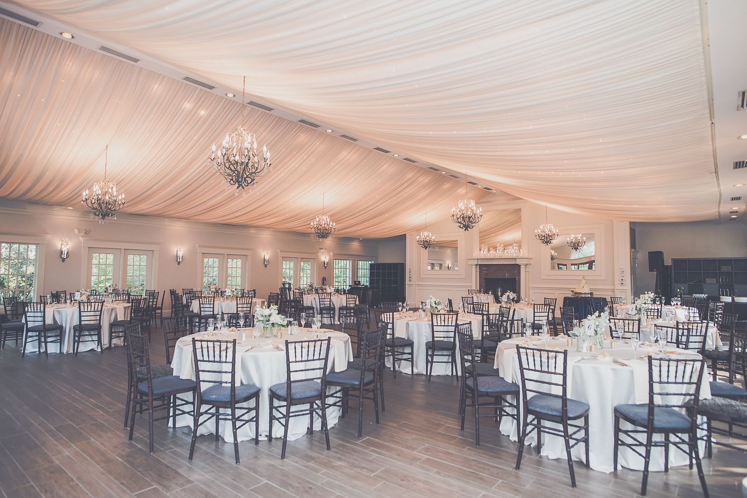 Elegant wedding reception venue with draped ceiling, chandeliers, and round tables.
