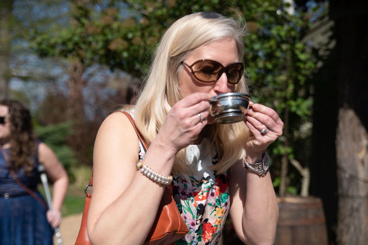 Elegant blonde woman sipping from a silver quaich cup at an outdoor Scottish-themed wedding.