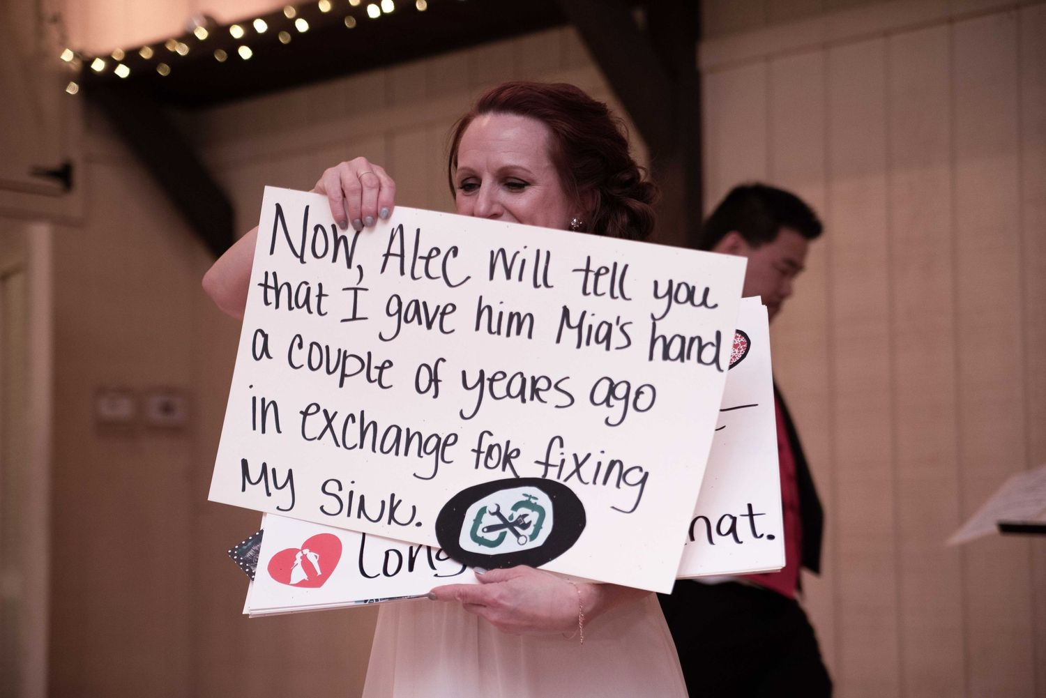 Woman holding handwritten sign at wedding reception about giving away bride in exchange for fixing her sink.