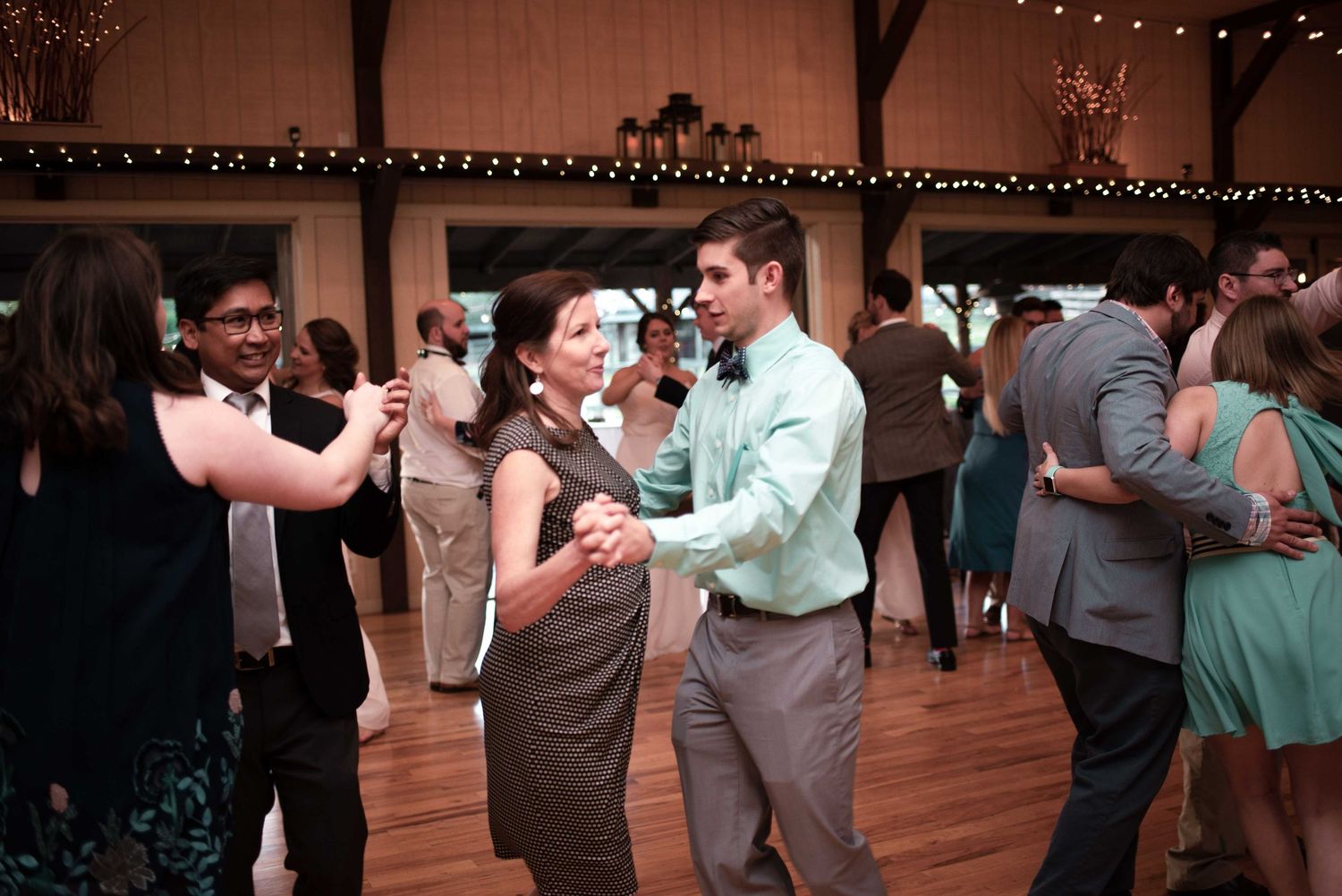 Couples dancing at elegant wedding reception in rustic barn venue with warm lighting.