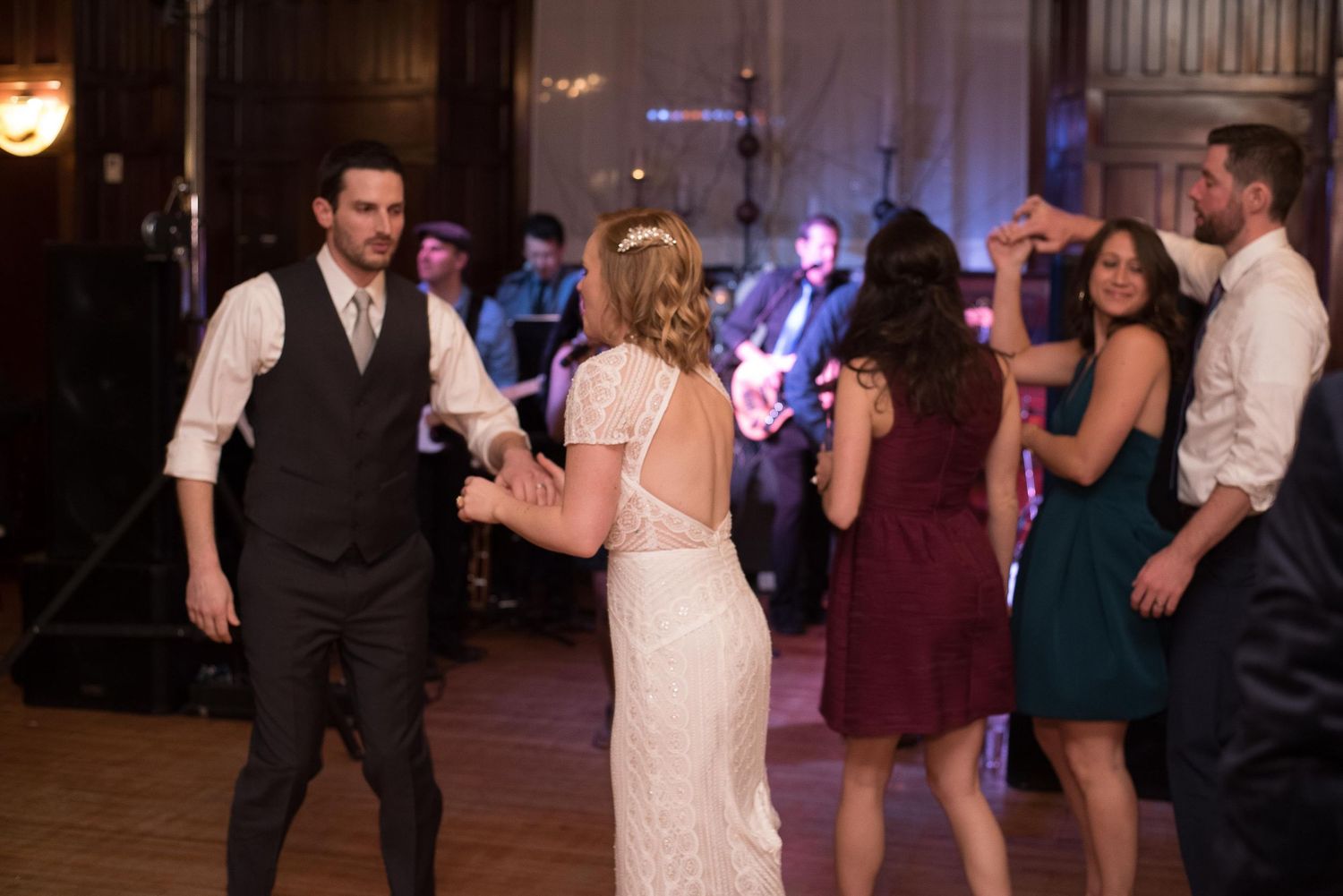 Bride and groom dancing with guests at a wedding reception in a grand venue.