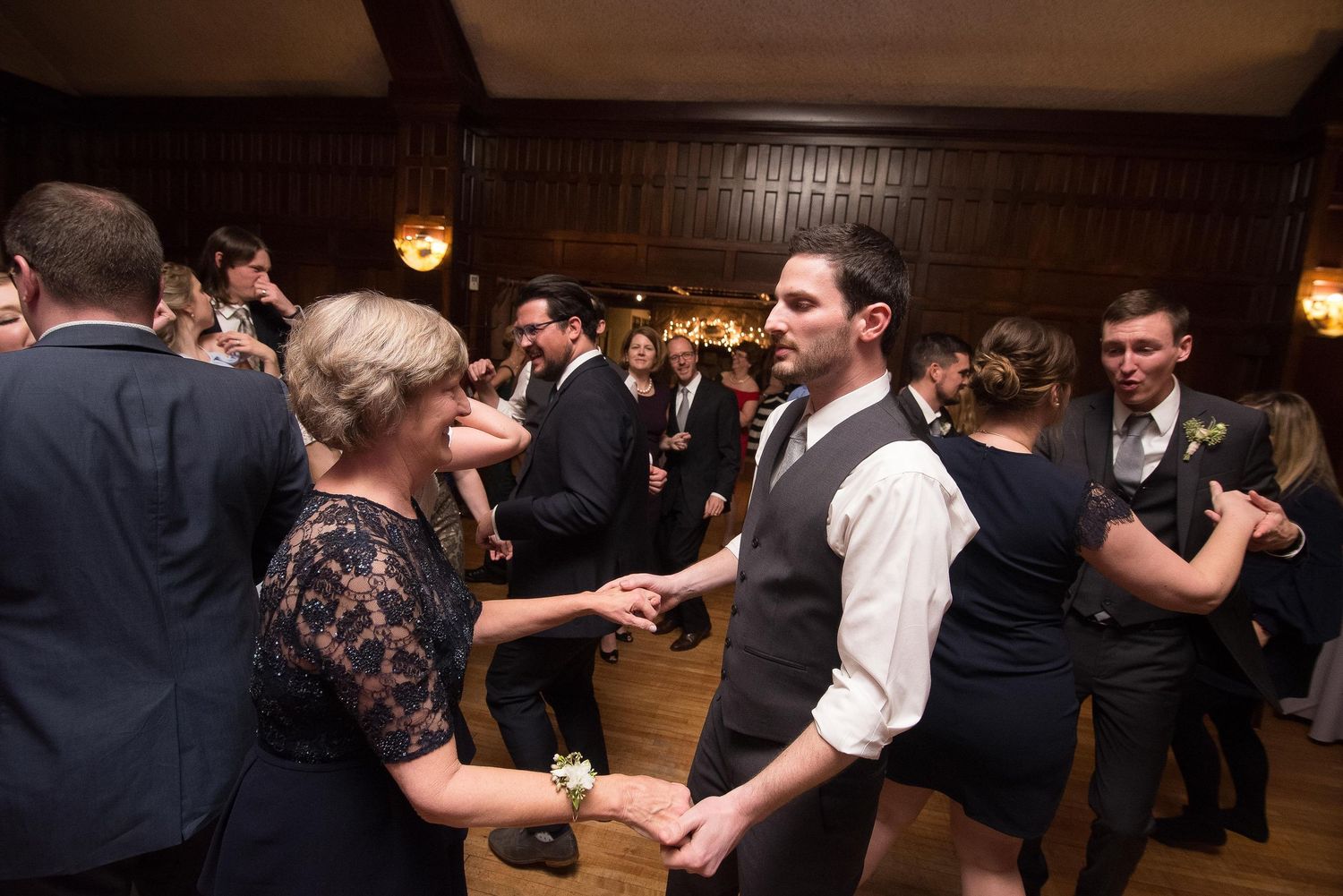 Guests dancing at a formal wedding reception in an elegant wood-paneled ballroom.