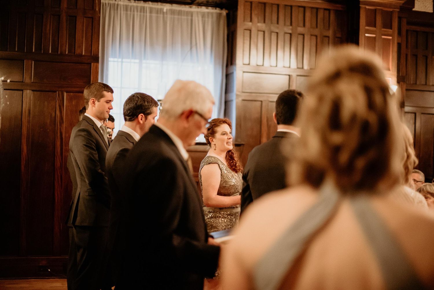 Guests mingling in an elegant wood-paneled venue during a wedding reception gathering.