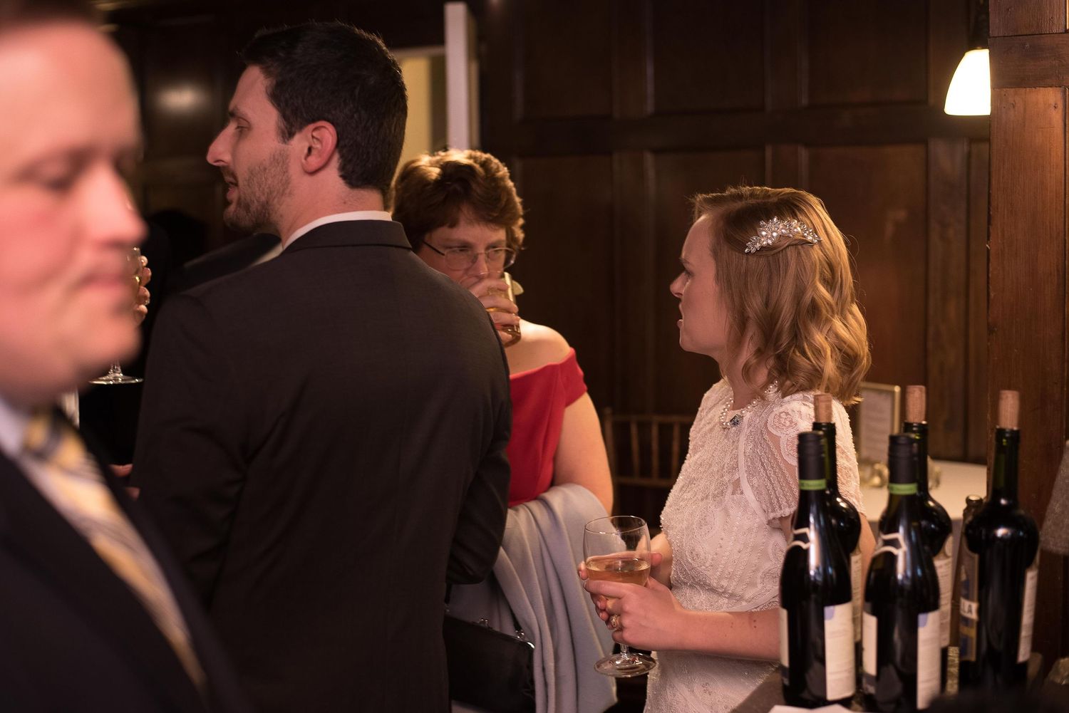 Elegant guests socializing at a formal evening event with wine bottles displayed on a bar counter.