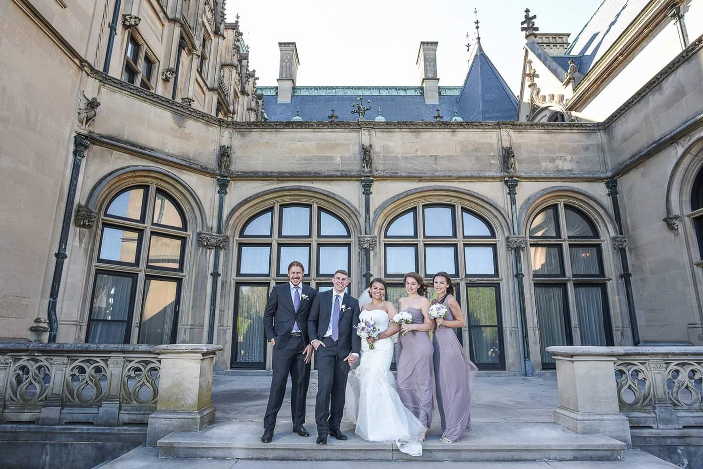 Small wedding party posing on steps of grand historic stone building.