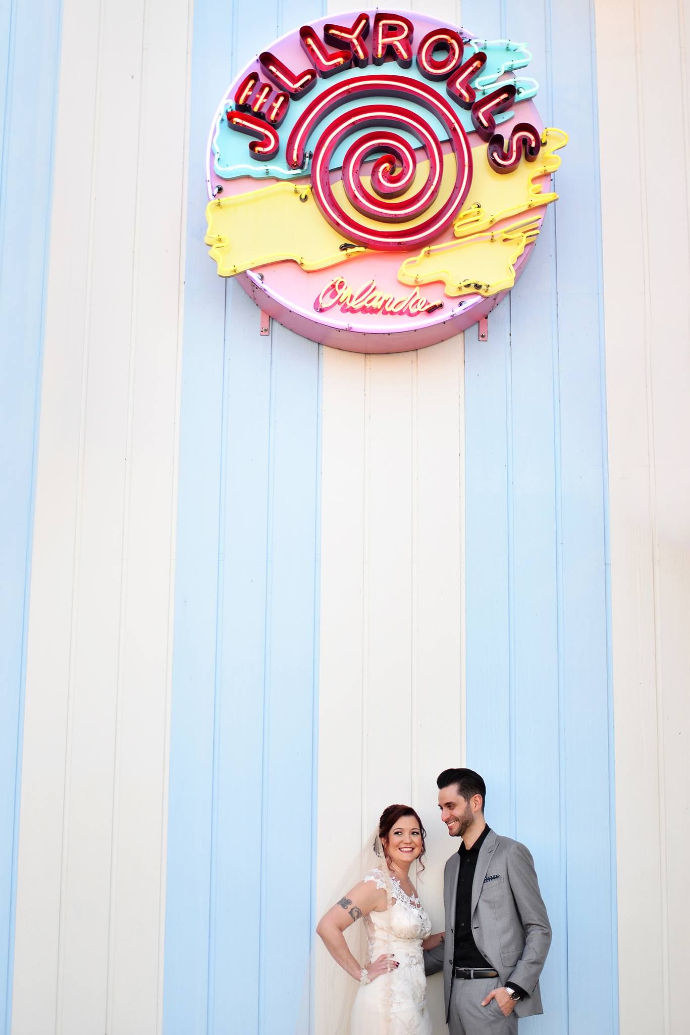 Bride and groom posing under colorful Jellyrolls neon sign at Disney resort.