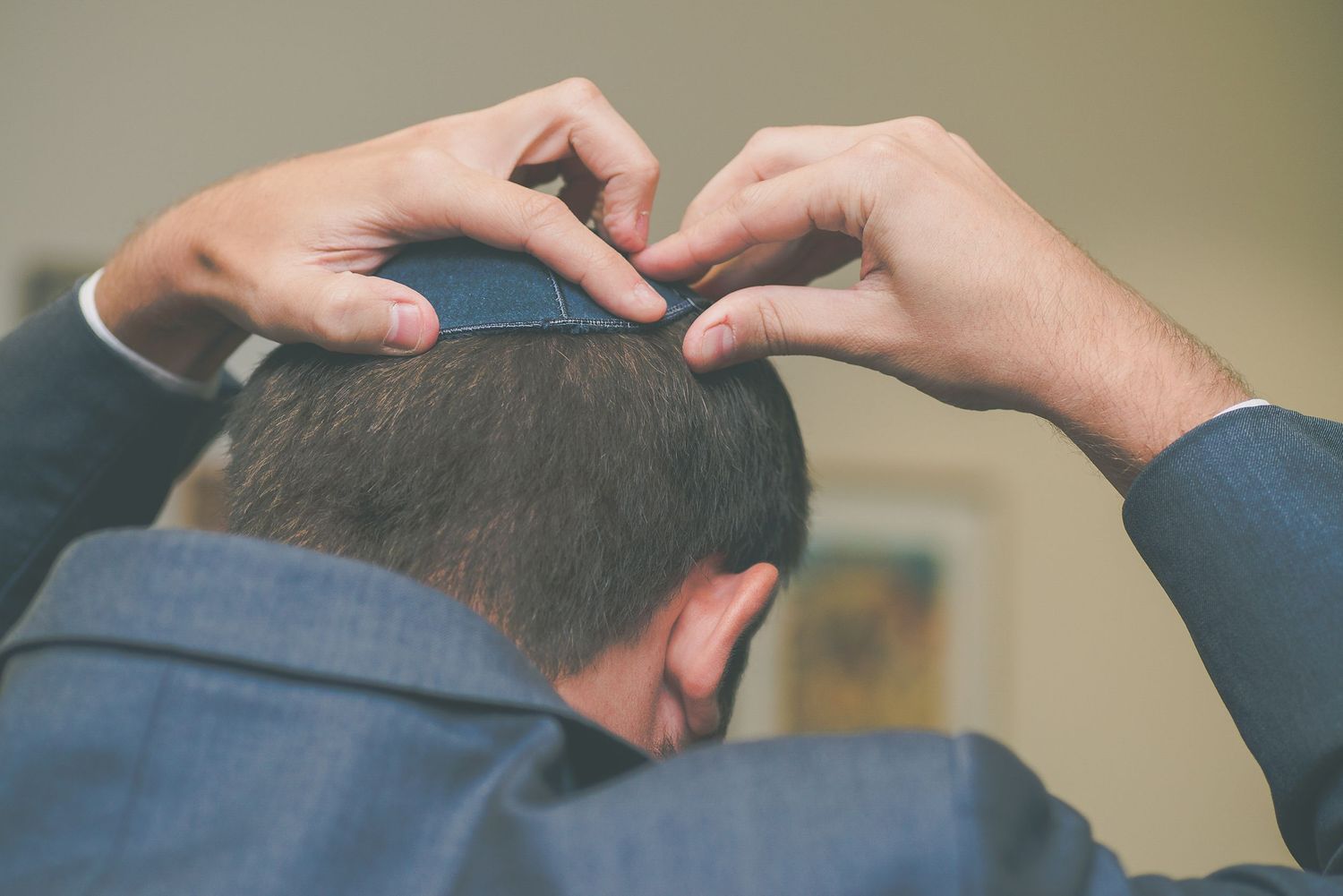 Groom placing a kippah on his head while preparing for a Jewish wedding ceremony.